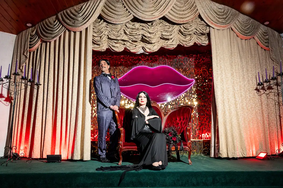 Gomez and Morticia Addams character impersonators posing on the gothic-themed stage set at Viva Las Vegas Weddings