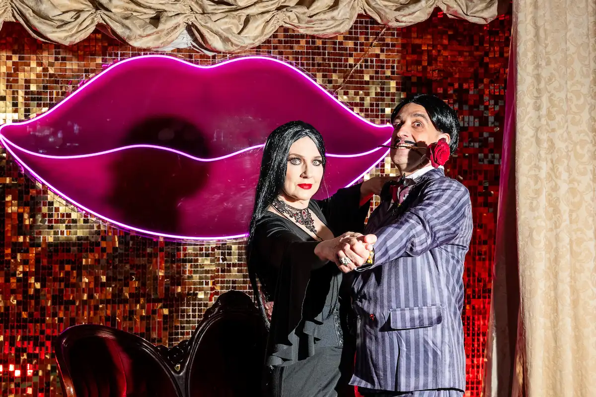 Gomez and Morticia Addams character impersonators dancing in front of the neon lips backdrop at Viva Las Vegas Weddings
