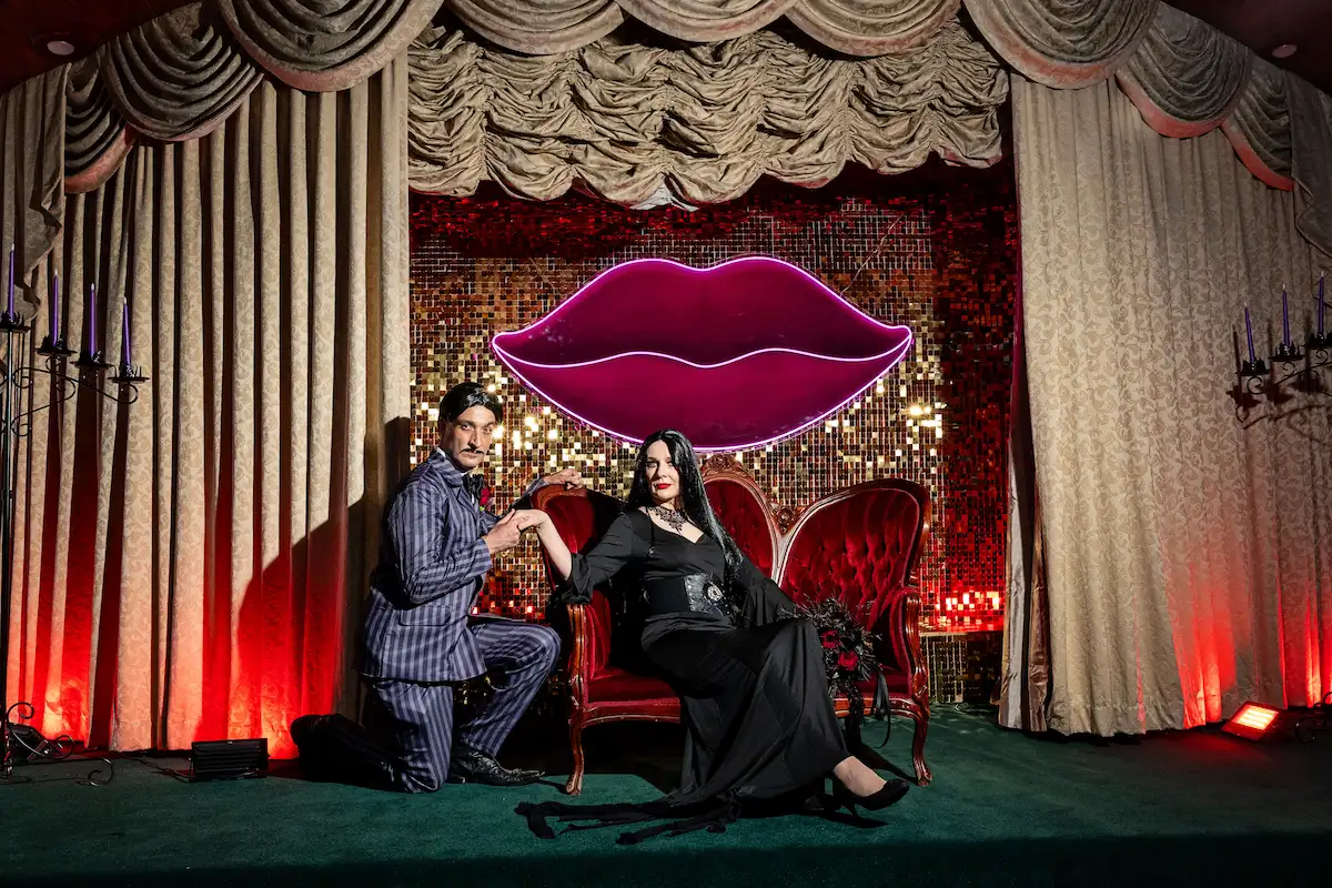 Gomez and Morticia Addams character impersonators standing beside the red velvet chairs on the gothic wedding stage at Viva Las Vegas Weddings