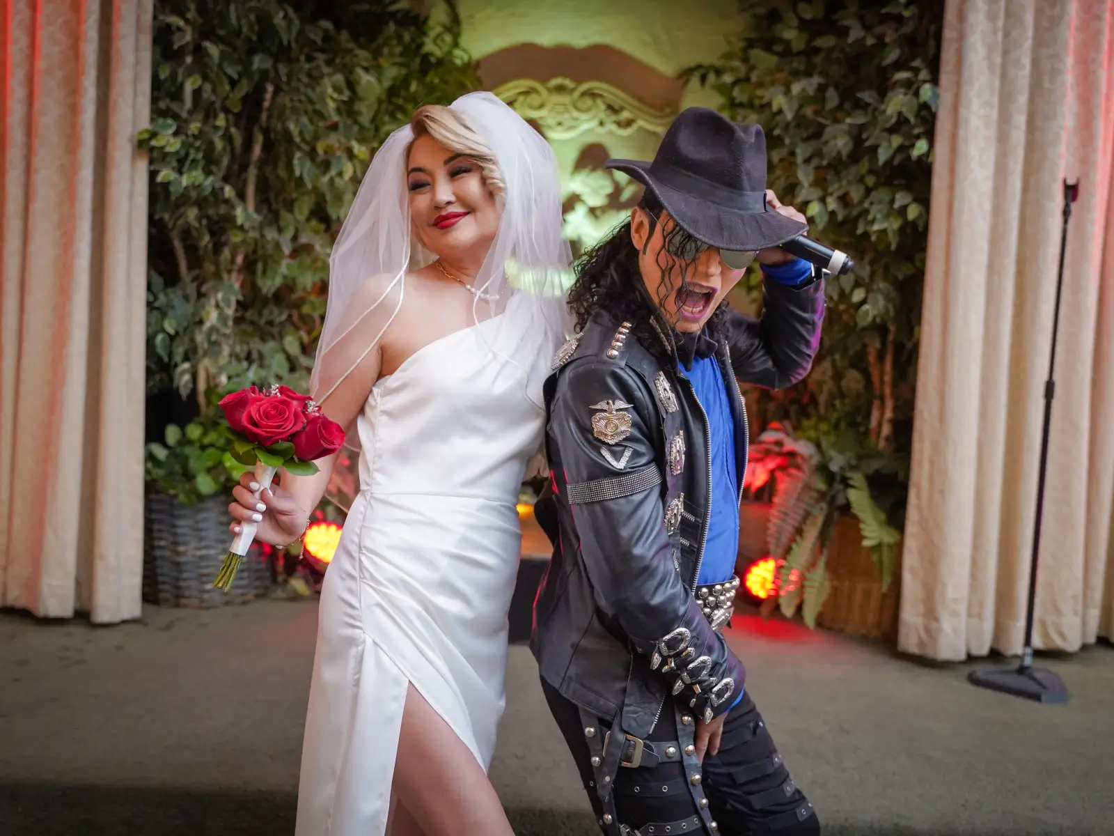 Bride with red rose bouquet poses back to back with Michael Jackson impersonator in leather jacket at Las Vegas wedding