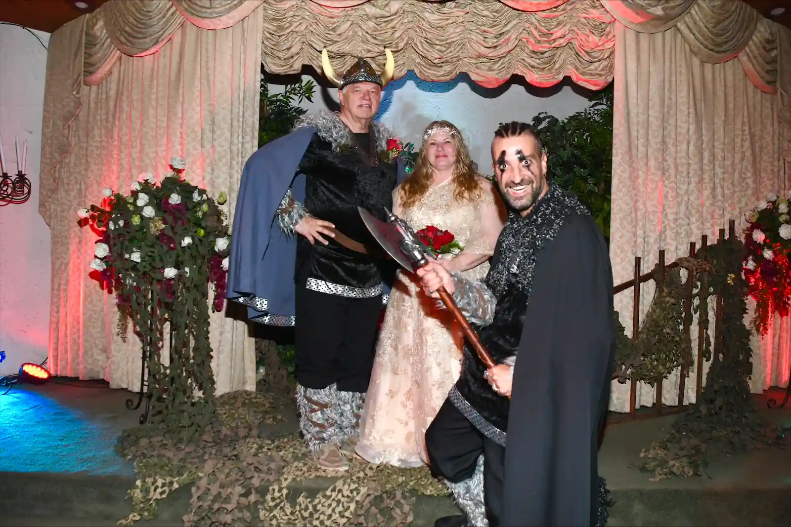 Viking themed wedding couple in horned helmet and gold gown pose with warrior officiant holding battle axe at Las Vegas chapel