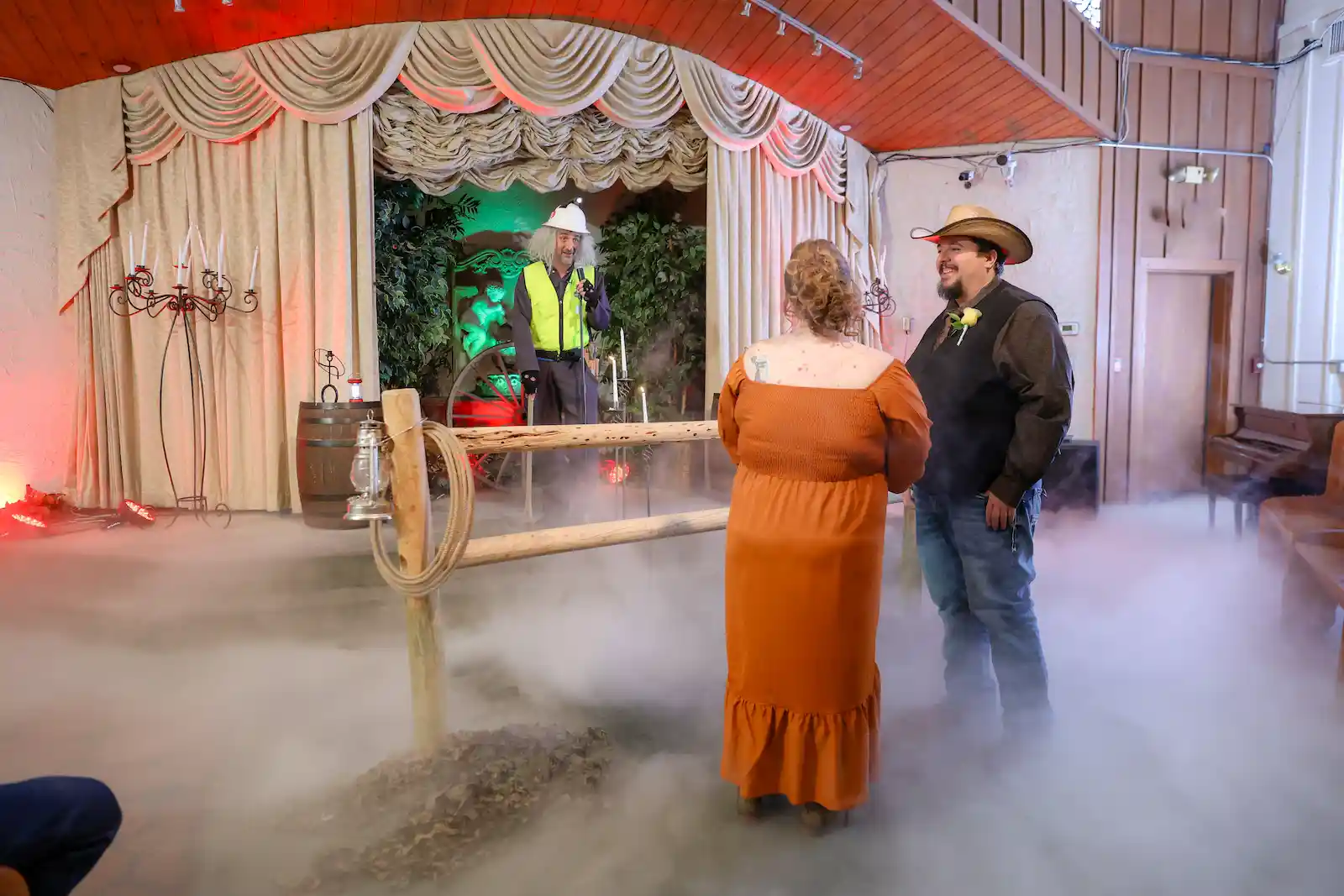Bride in orange dress and cowboy groom stand in dry ice fog during western themed wedding at Las Vegas chapel