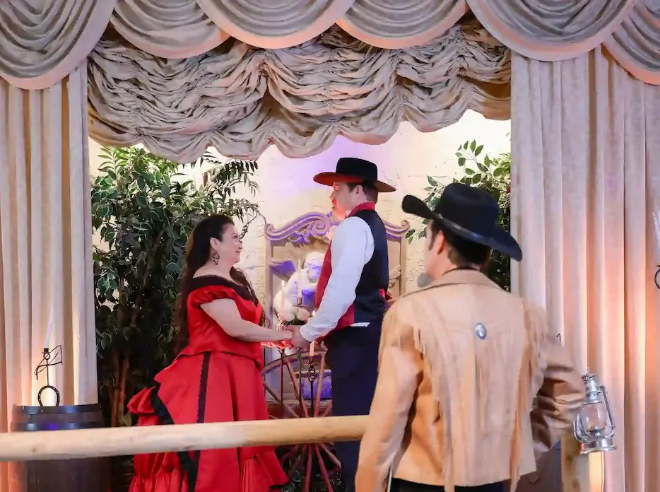 Bride in red saloon dress holds hands with cowboy groom during western themed wedding ceremony in Las Vegas
