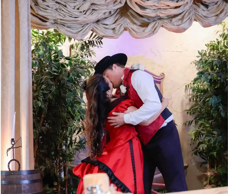 Bride in red saloon dress and cowboy groom share first kiss next to barrel and lasso at Las Vegas western wedding