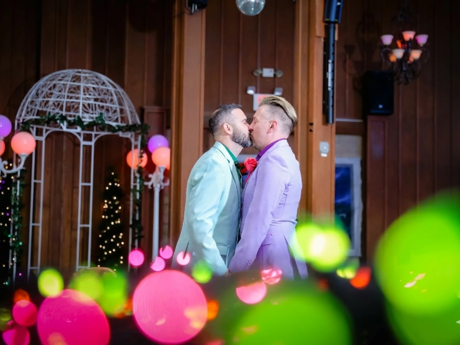 Two grooms sharing a first kiss at Viva Las Vegas Wedding Chapel with colorful bokeh lights.