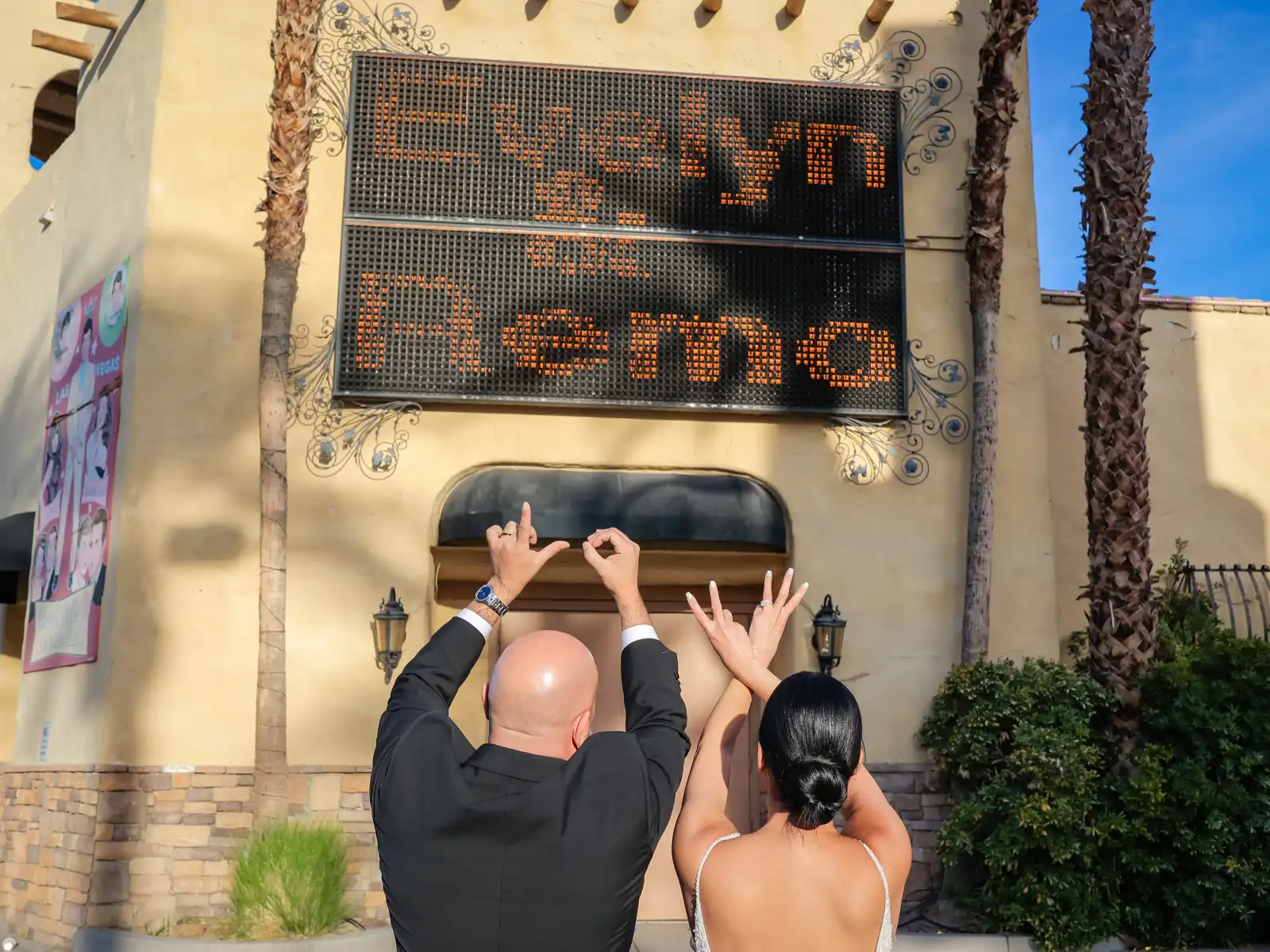 Newlywed couple cheering in front of the Viva Las Vegas Wedding Chapel marquee sign.