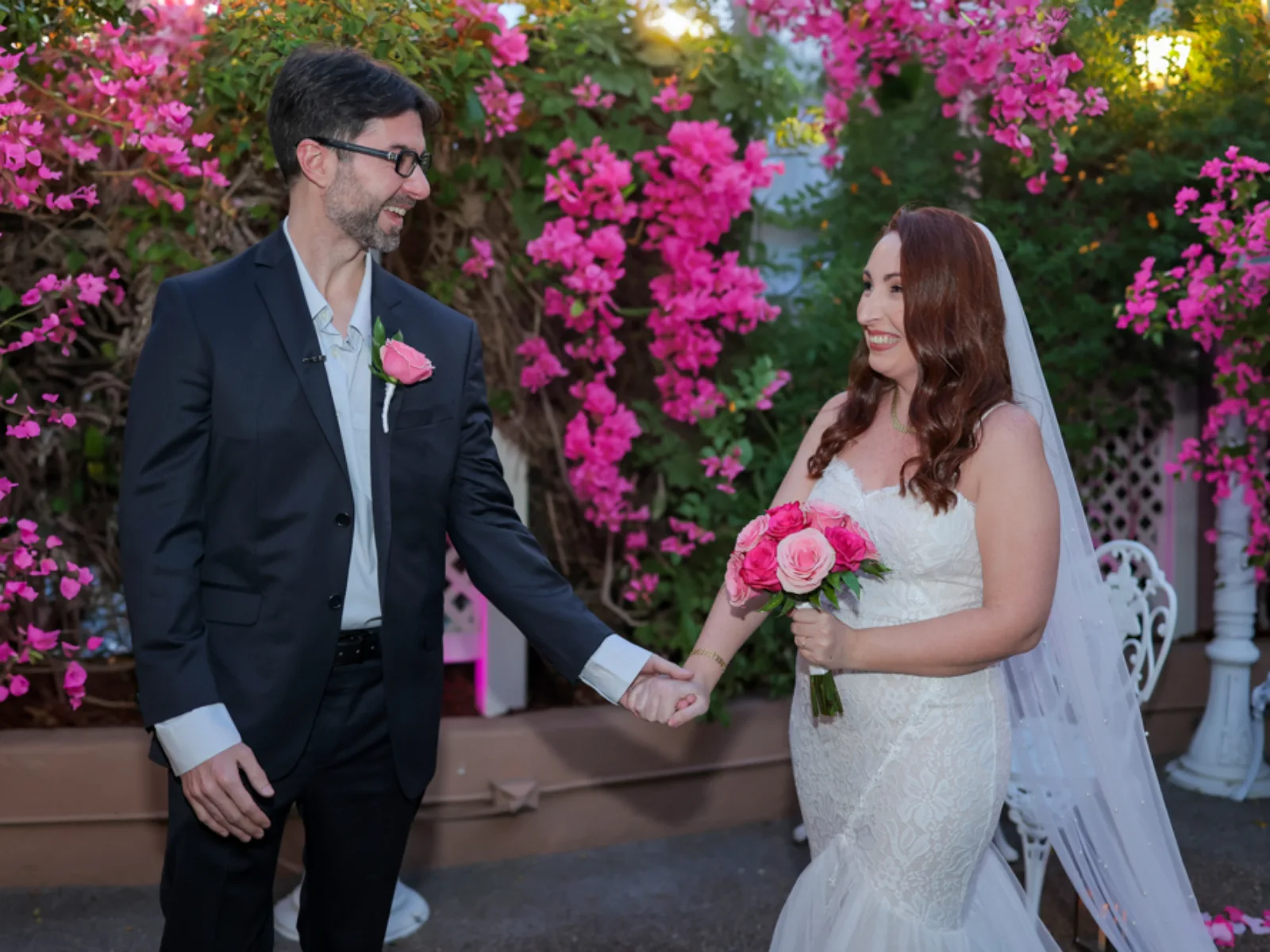 A romantic night shot of a bride and groom gazing at each other inside a white garden gazebo decorated with warm fairy lights and surrounded by greenery.