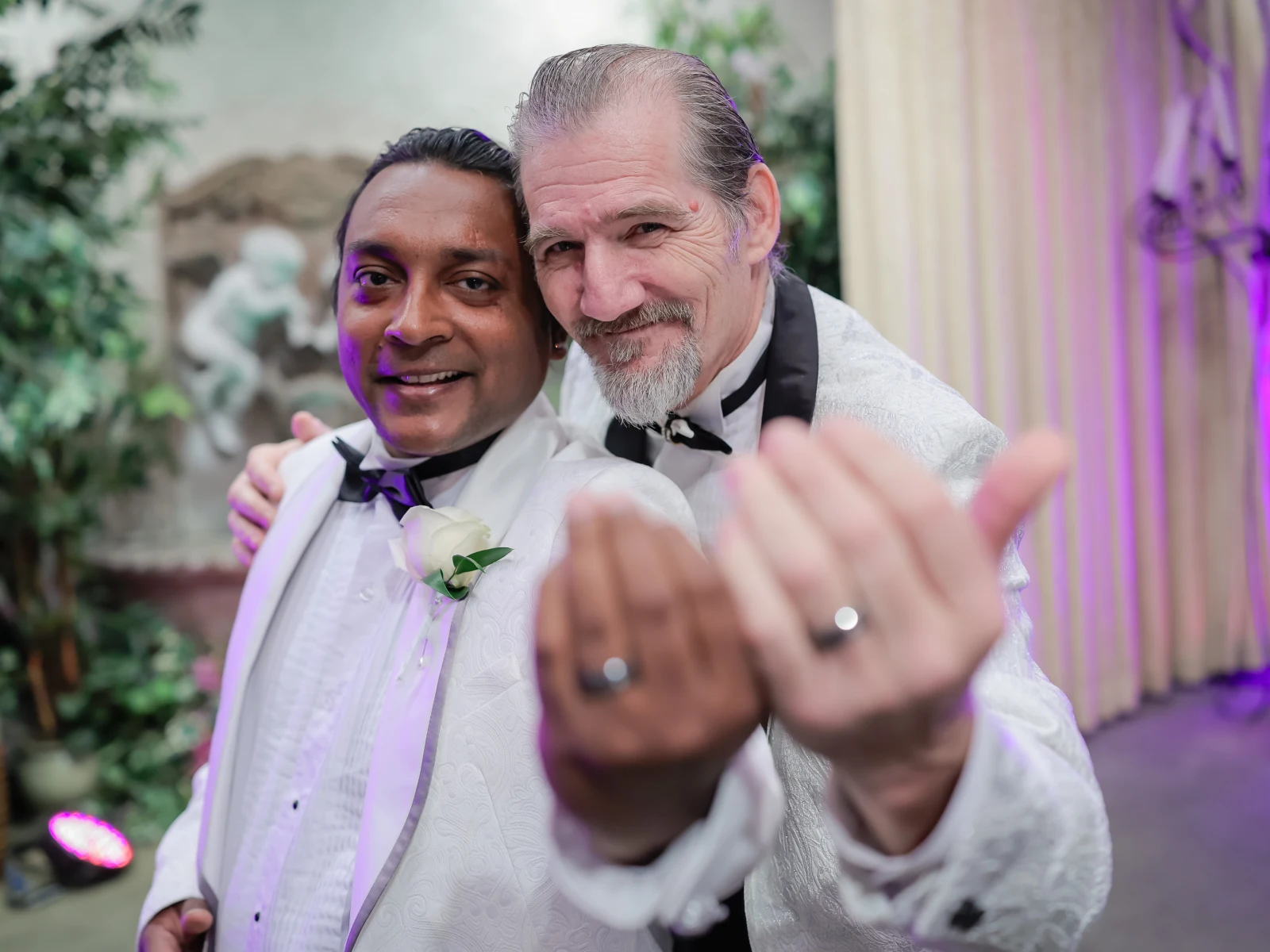 Two grooms in white tuxedos showing wedding rings during Las Vegas ceremony.