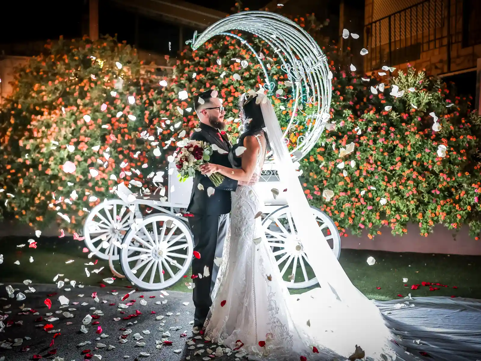 A wide night portrait of a bride and groom in an illuminated garden; the bride