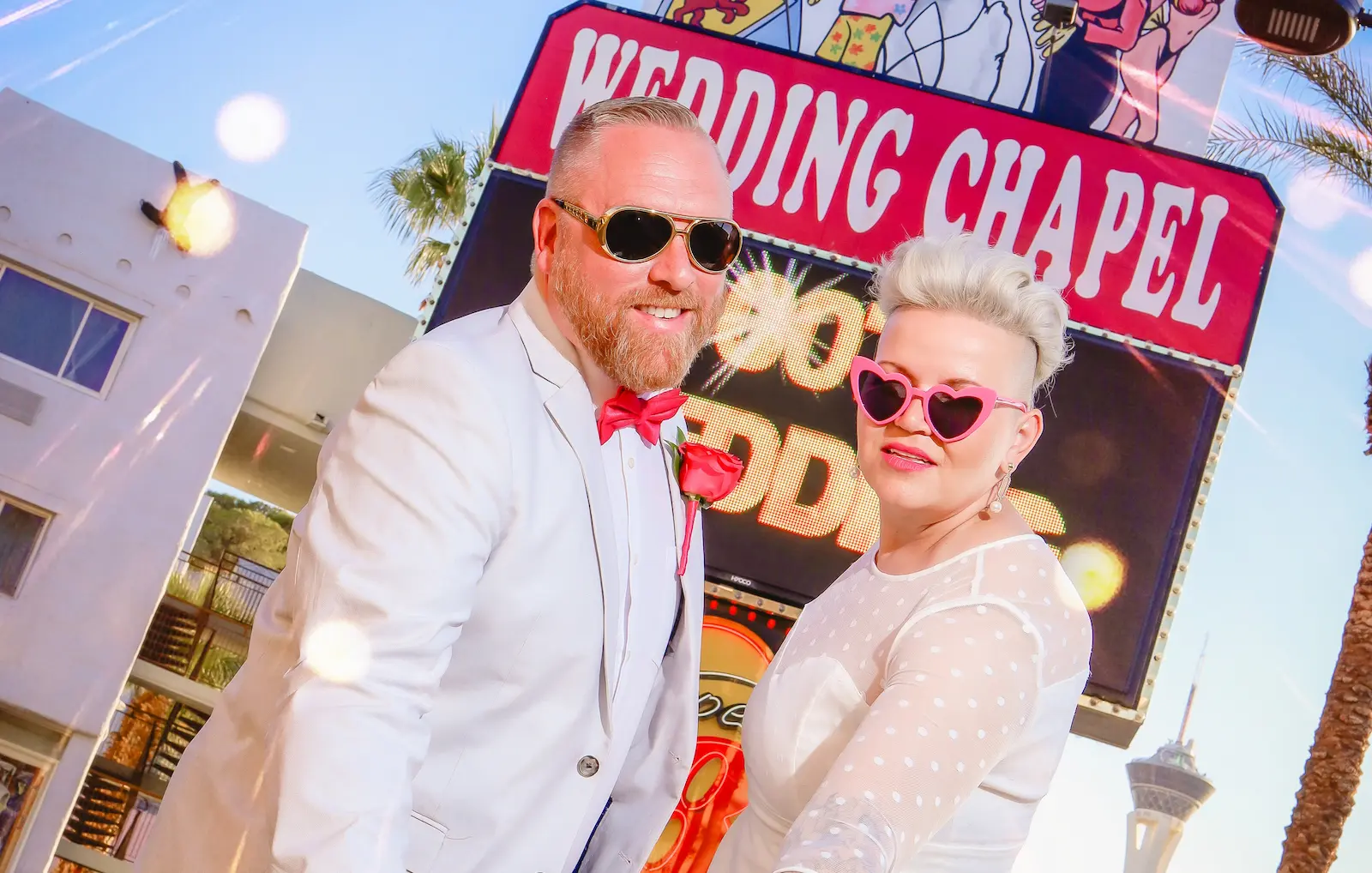 Couple wearing heart sunglasses posing in front of Las Vegas wedding chapel sign