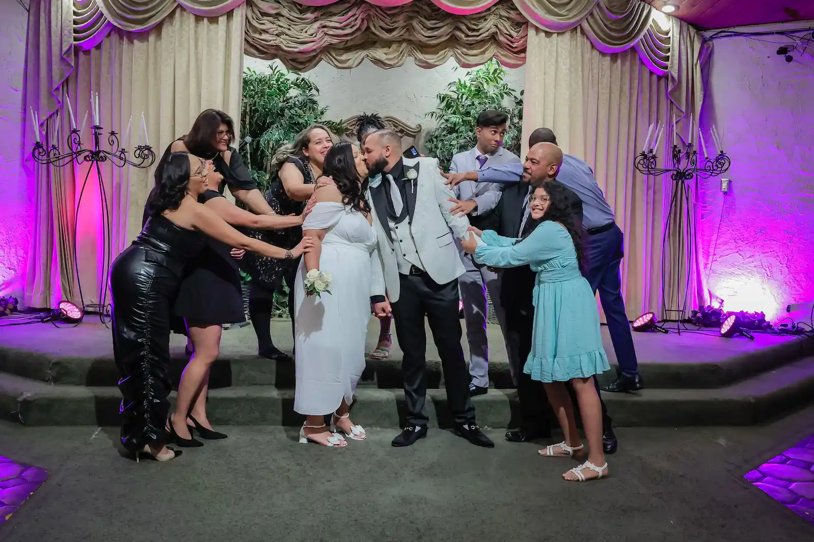 Bride and groom sharing a kiss surrounded by cheering family members at Viva Las Vegas Wedding Chapel.
