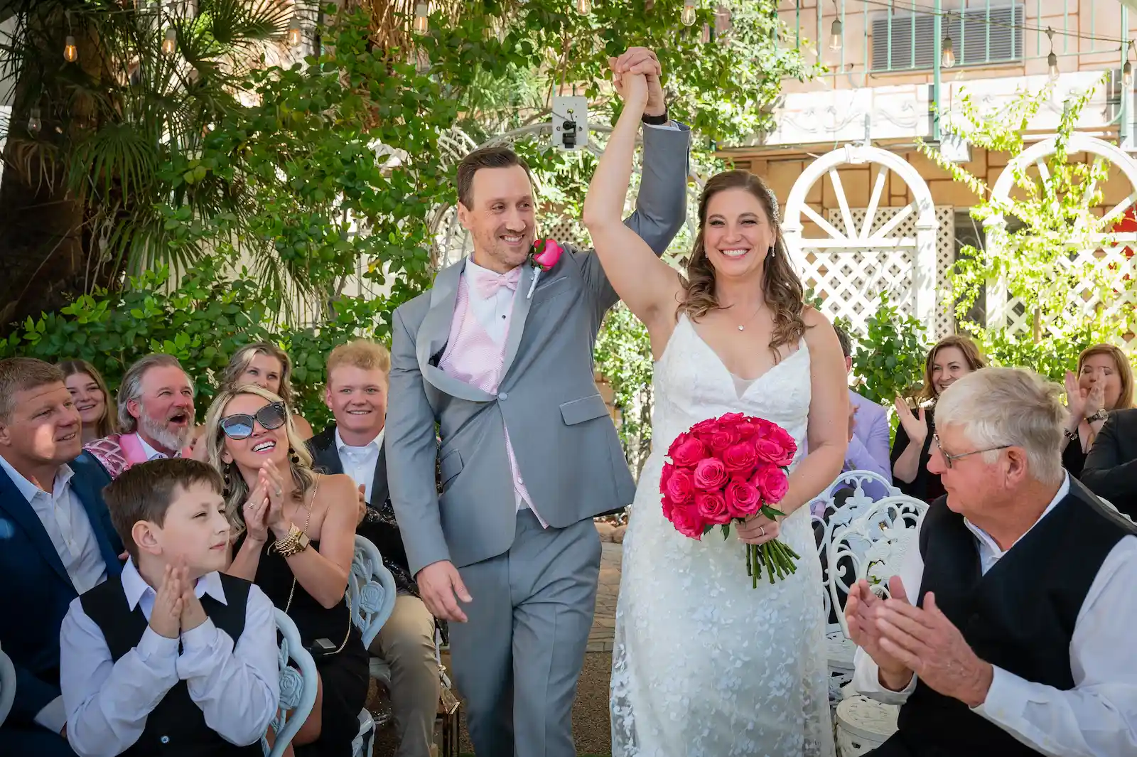 Bride and groom raising hands in celebration during recessional with cheering guests at Viva Las Vegas Wedding Chapel.