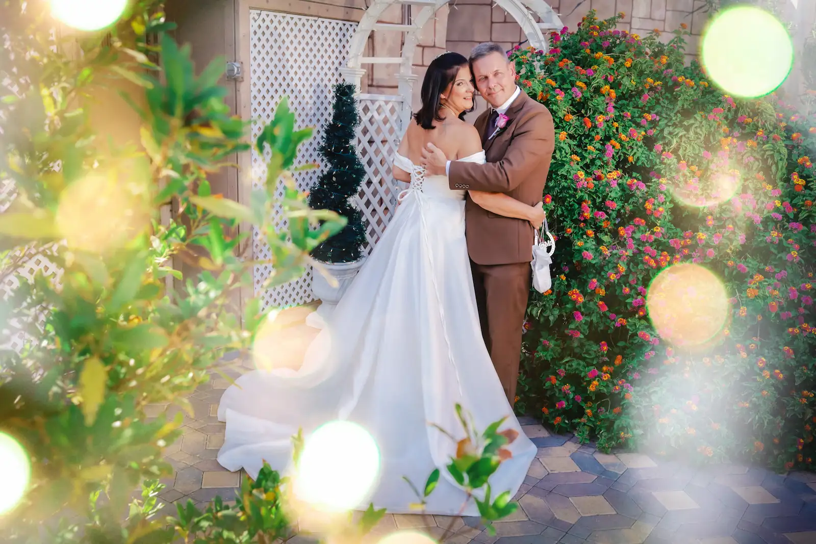 Bride and groom embracing in front of a vibrant orange and pink flower wall at Viva Las Vegas Wedding Chapel.