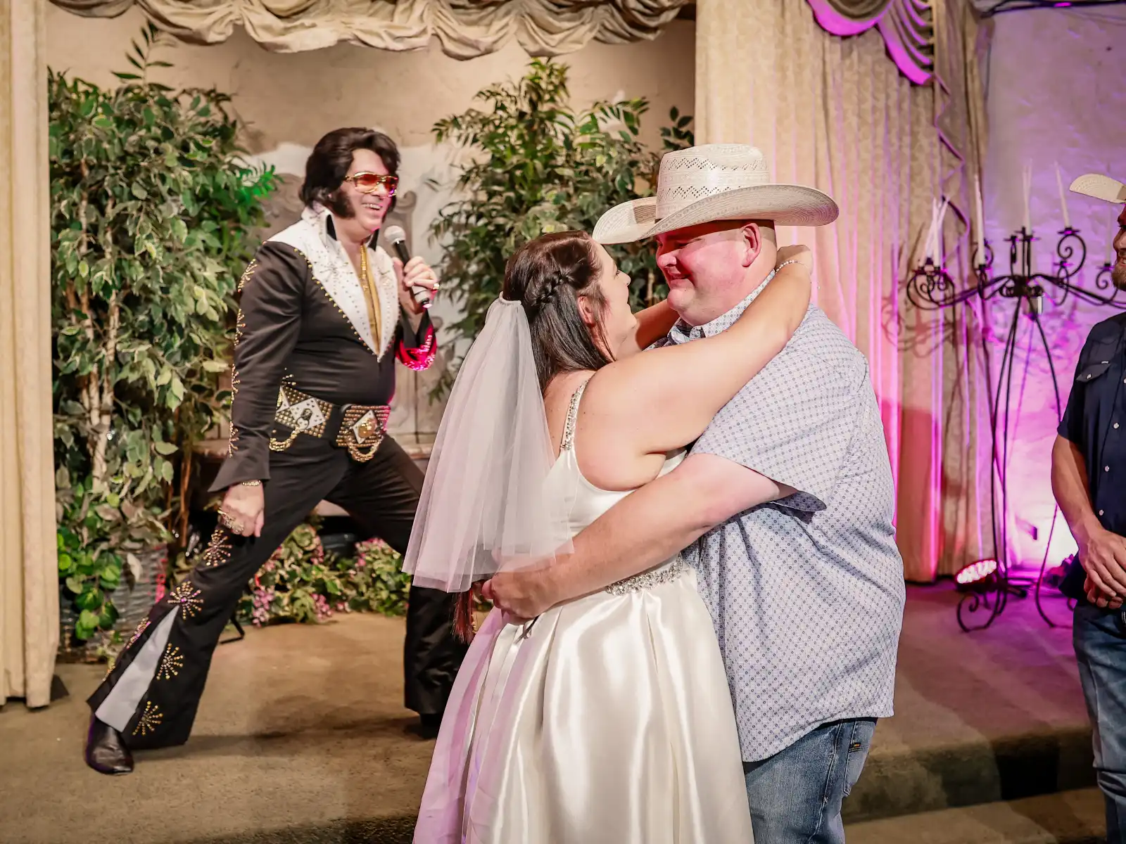 Fun Las Vegas Elvis wedding first dance with bride and groom embracing in chapel while Elvis impersonator performs live on stage