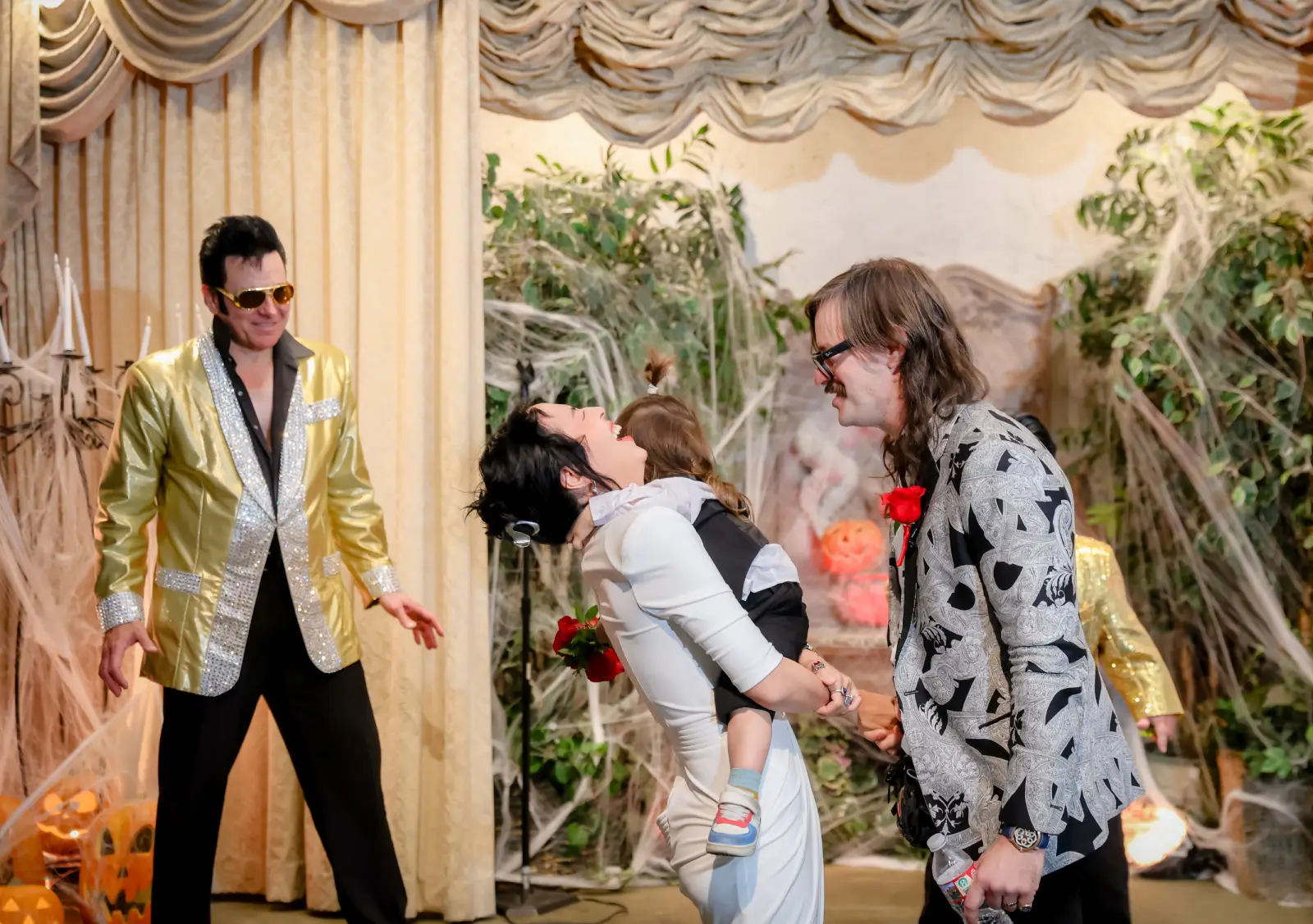 Fun themed Las Vegas Elvis wedding ceremony with couple holding hands and playful dip while Elvis impersonator performs in decorated chapel setting