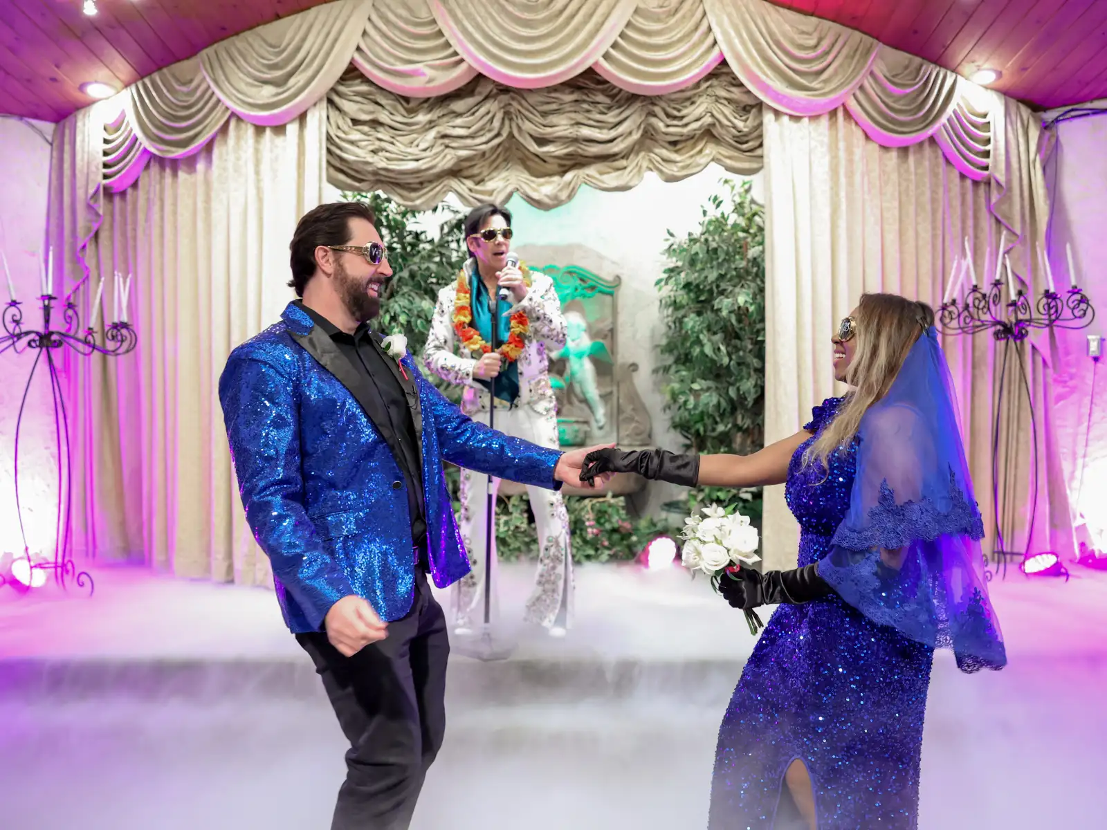 Glamorous Las Vegas Elvis wedding first dance with stylish bride and groom in blue outfits surrounded by romantic fog in elegant chapel ceremony