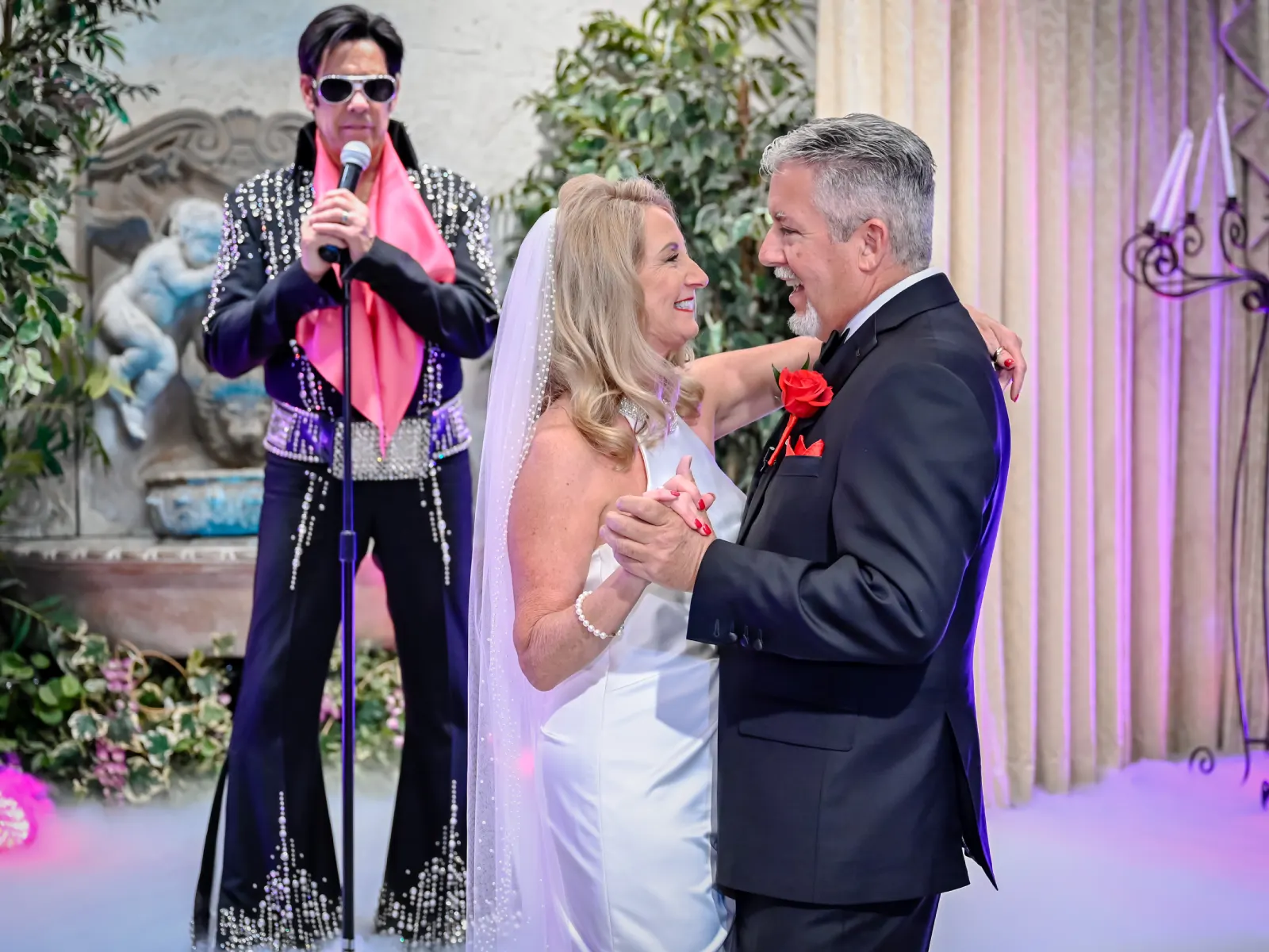 Romantic Las Vegas Elvis wedding first dance with smiling bride and groom embracing in elegant chapel while Elvis impersonator sings live on stage