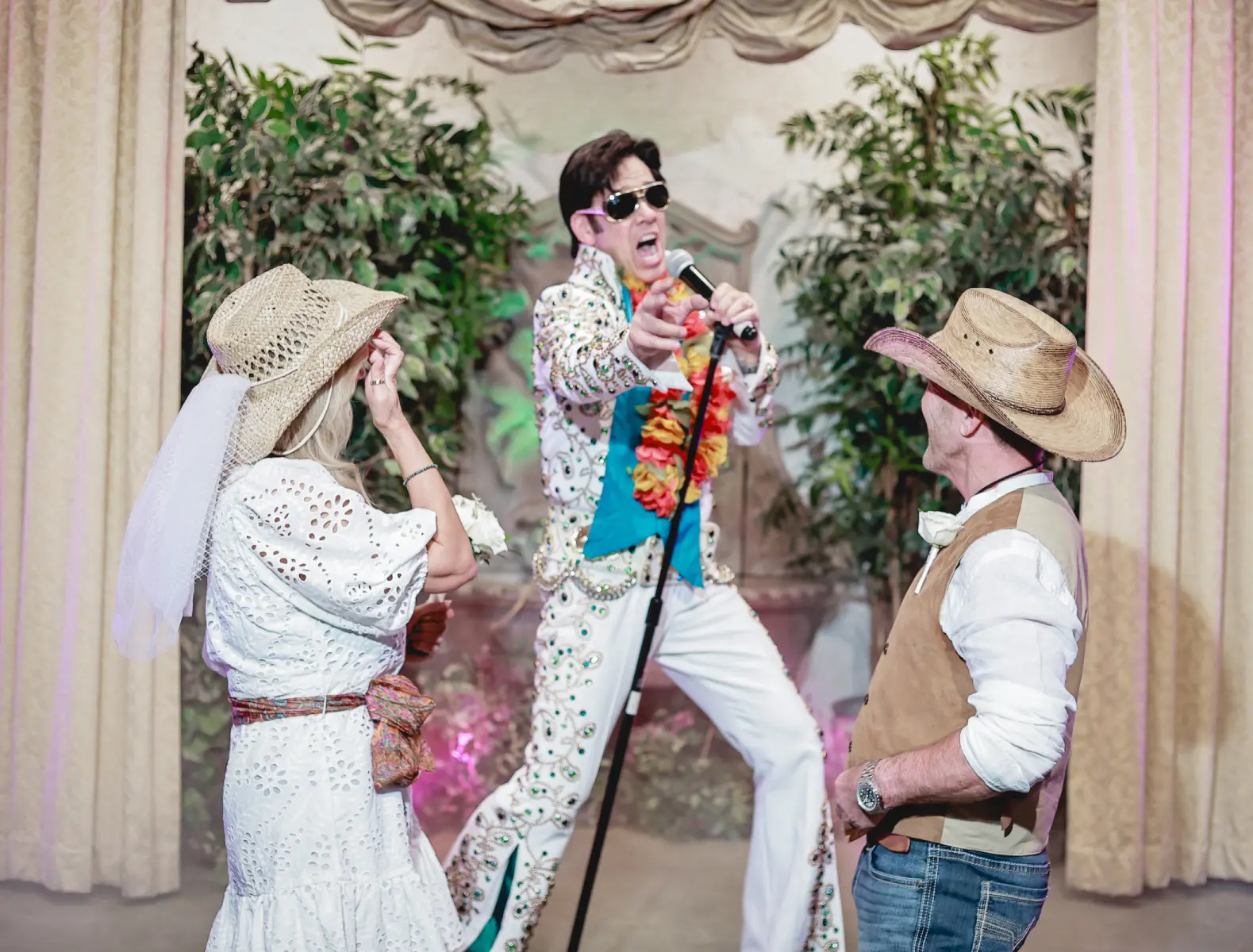 Fun country-style Las Vegas Elvis wedding moment with bride and groom in cowboy hats enjoying live performance during themed chapel ceremony