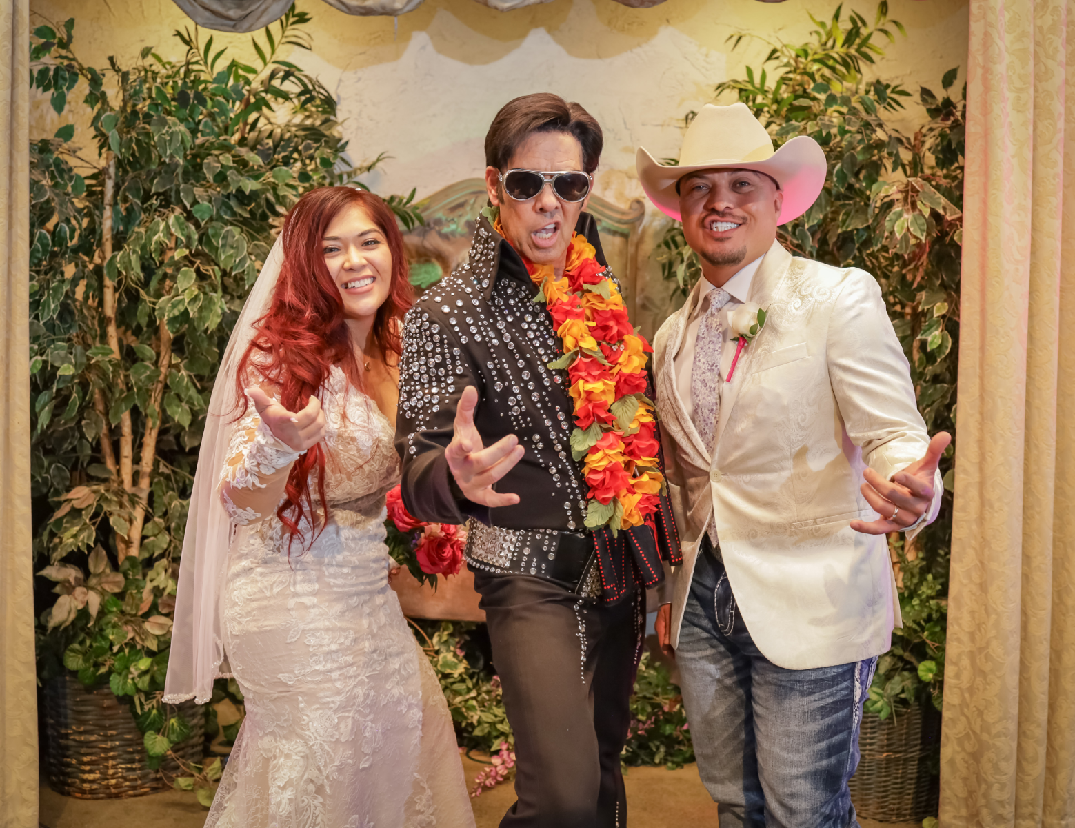 Fun Las Vegas Elvis wedding photo with red-haired bride, cowboy-hat groom and Elvis impersonator posing together inside romantic chapel ceremony setting