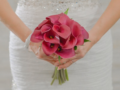 Elegant bridal bouquet of deep pink calla lilies held by bride in white wedding gown