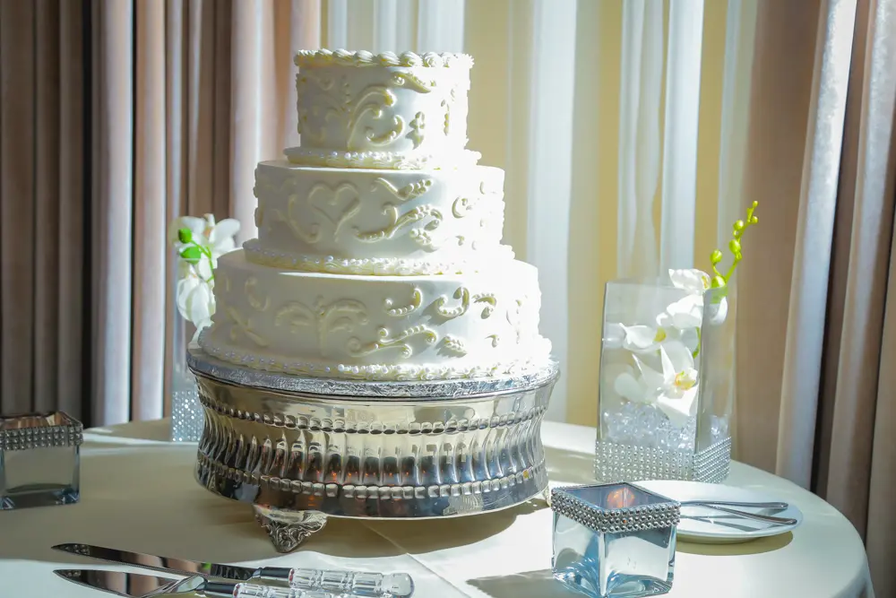 Three-tier white wedding cake with scroll detailing on silver stand