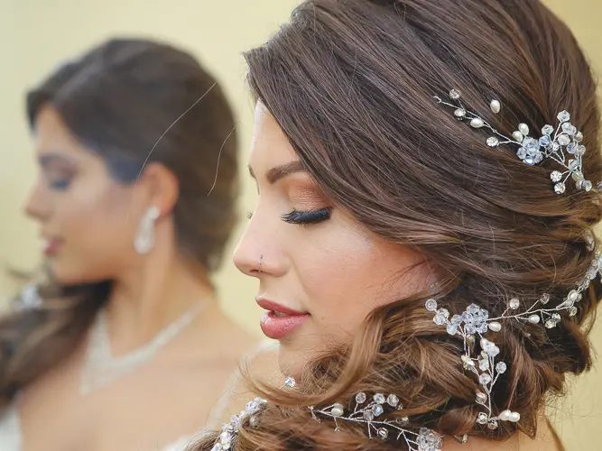 Bride with curled updo, crystal hair vine, and glam makeup ready for her wedding.