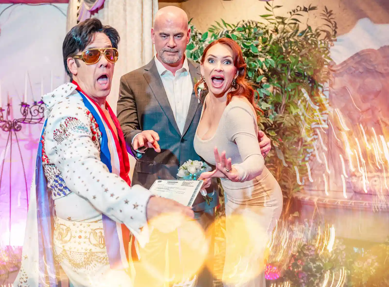 Elvis impersonator posing with surprised wedding couple holding marriage certificate at Las Vegas chapel