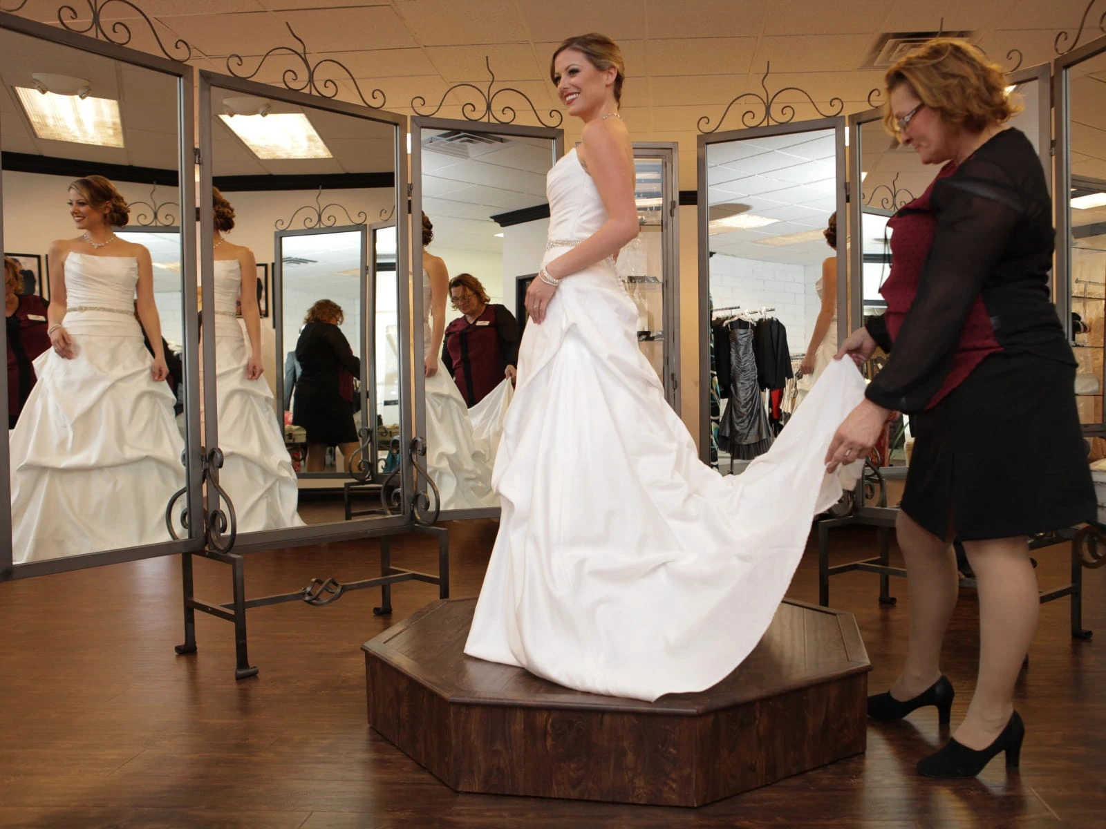 Bride trying on white satin wedding gown on fitting pedestal with three-way mirror at Las Vegas bridal shop