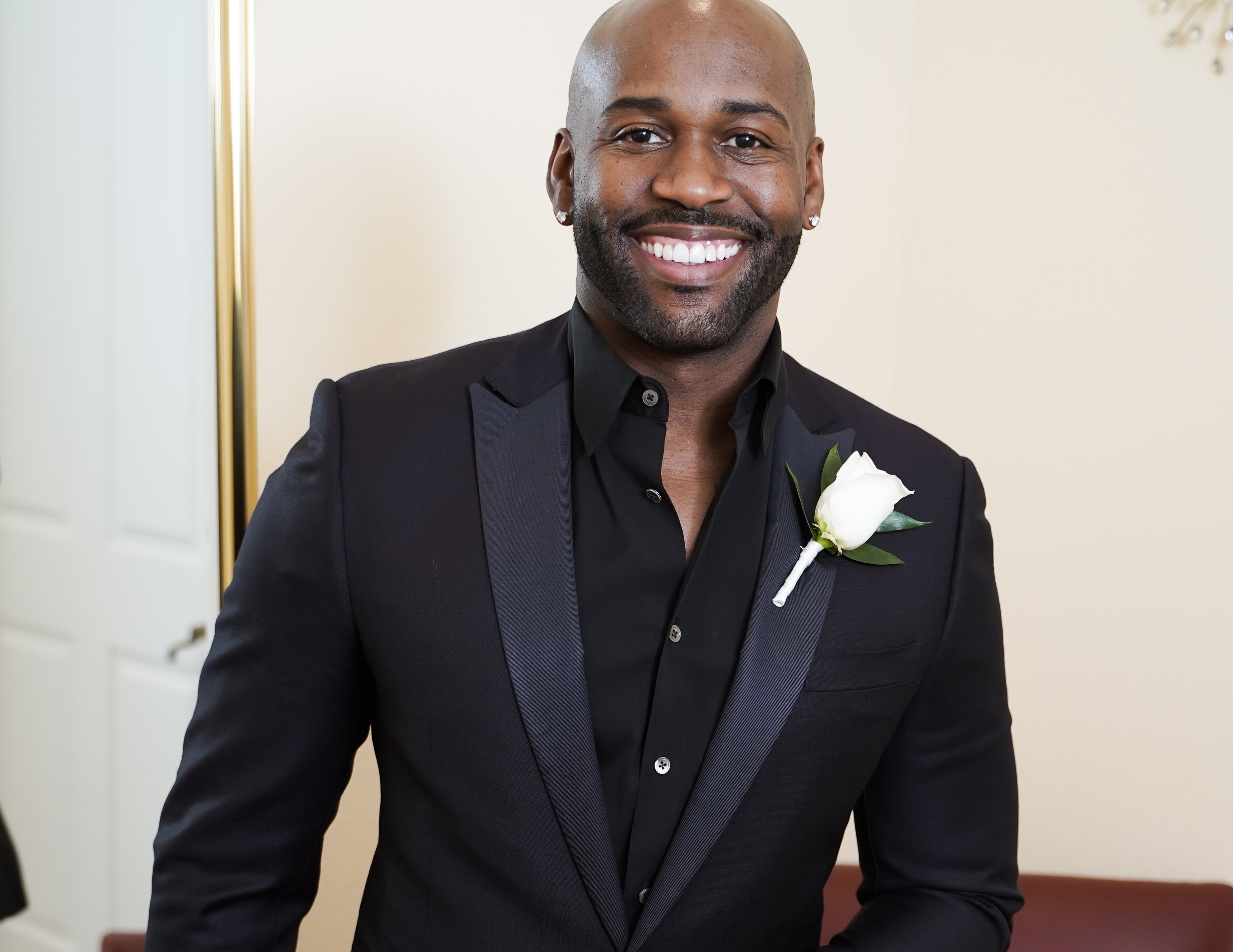 Groom in all-black tuxedo with white rose boutonniere