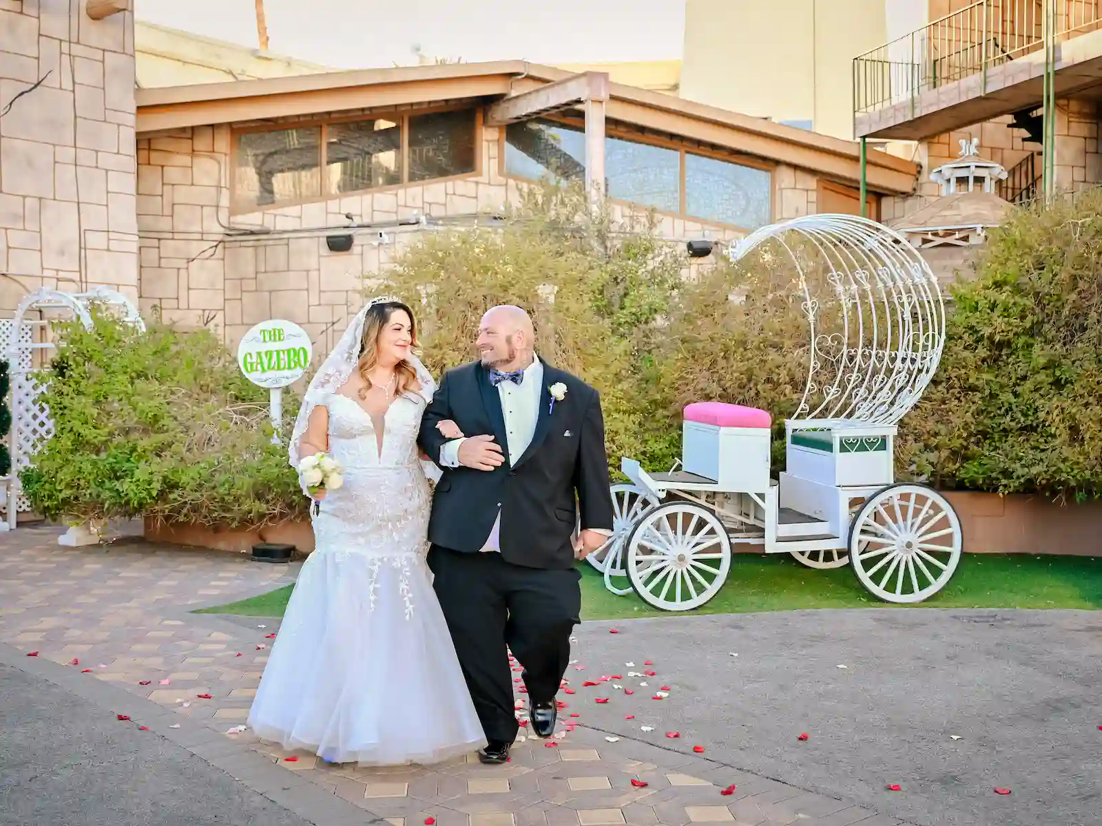 Wedding couple walking arm in arm past white carriage and rose petals