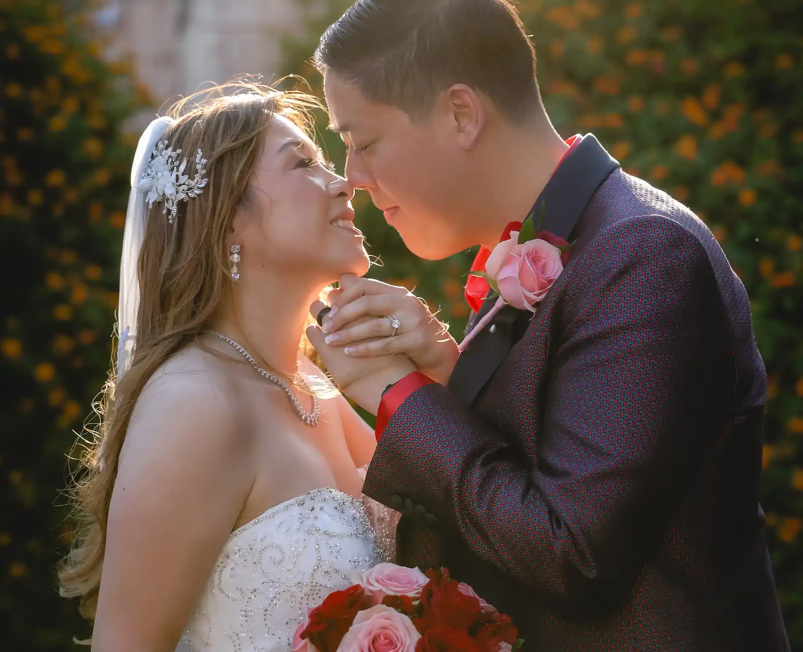 Bride and groom in golden sunset embrace with pink and red rose bouquet at Las Vegas outdoor wedding venue