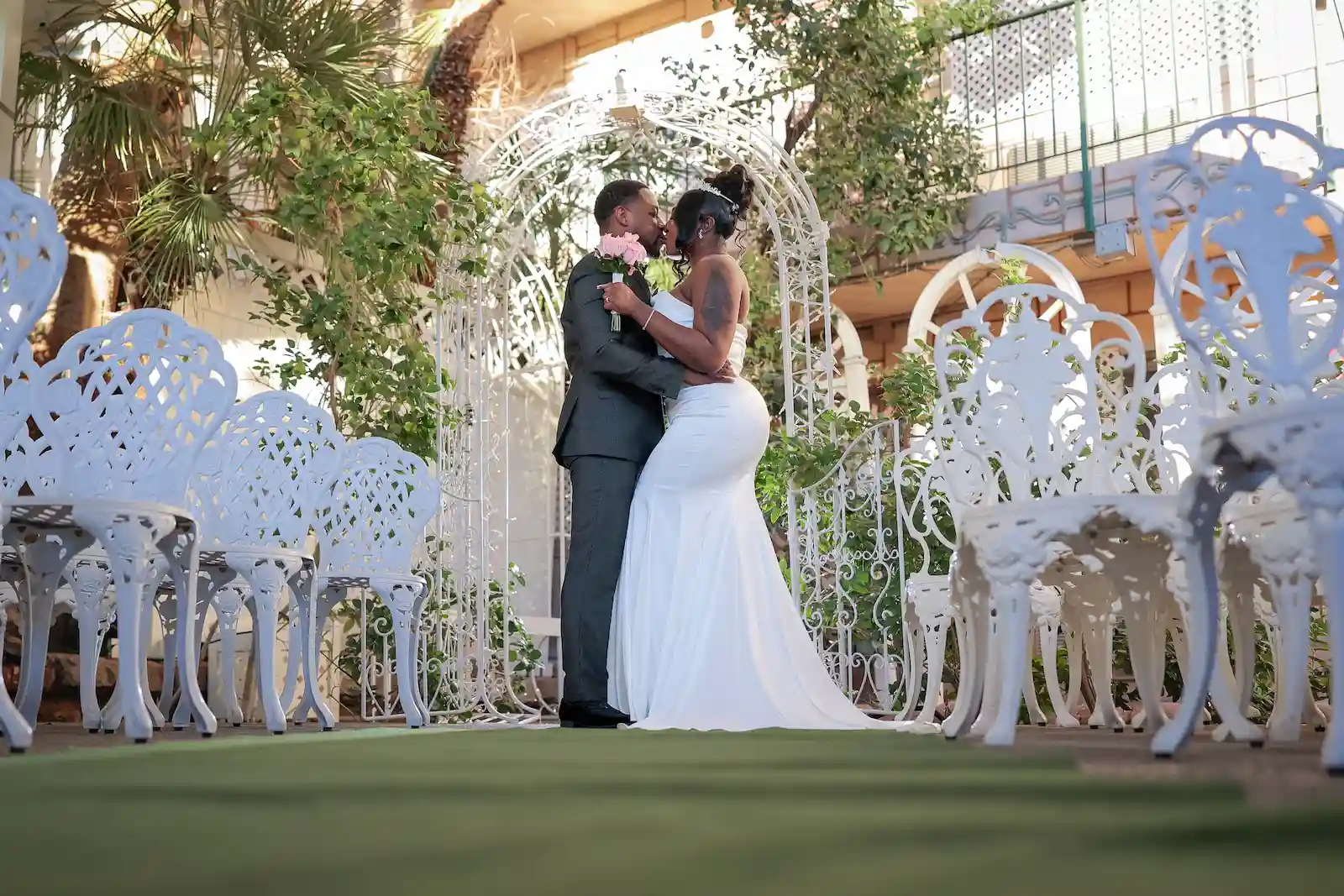 Bride and groom sharing first kiss under white garden arbor at Viva Las Vegas Wedding Chapel