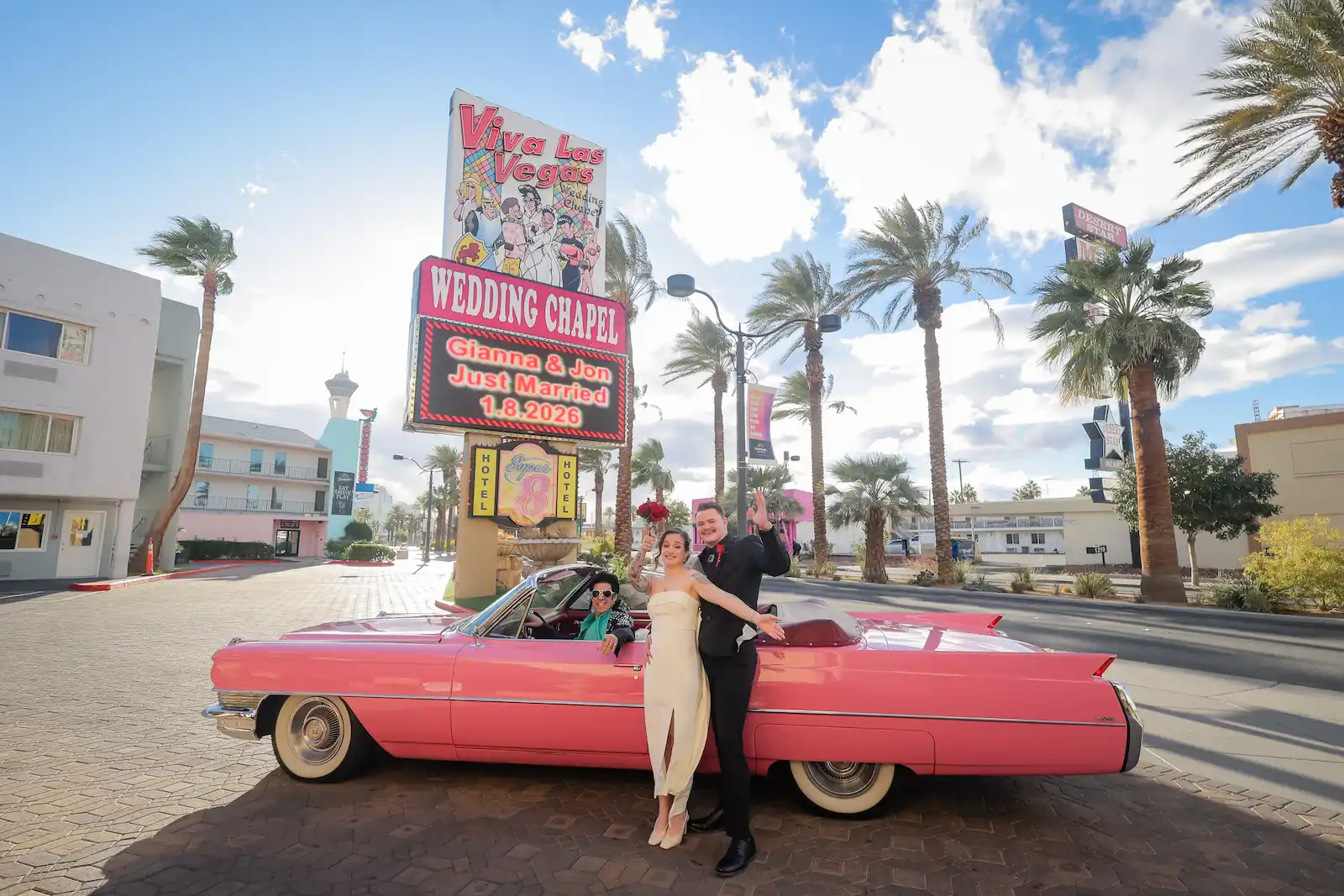 Just married couple posing with vintage pink Cadillac in front of Viva Las Vegas Wedding Chapel billboard sign