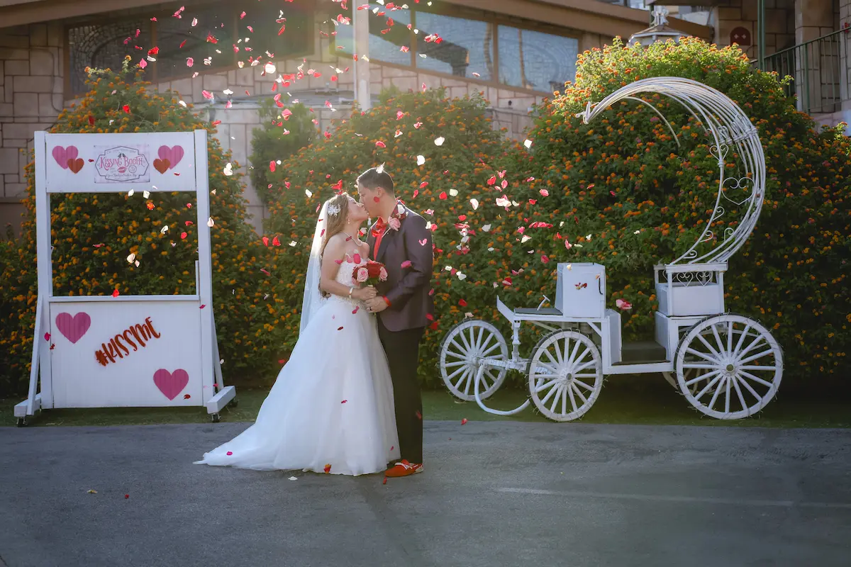 Bride and groom kissing with rose petals falling beside kissing booth and Cinderella carriage at Viva Las Vegas