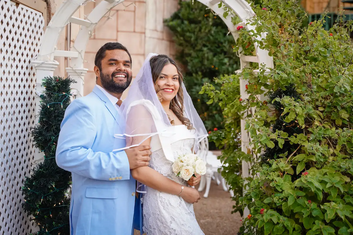 Smiling newlyweds posing under white garden arbor at Viva Las Vegas Wedding Chapel