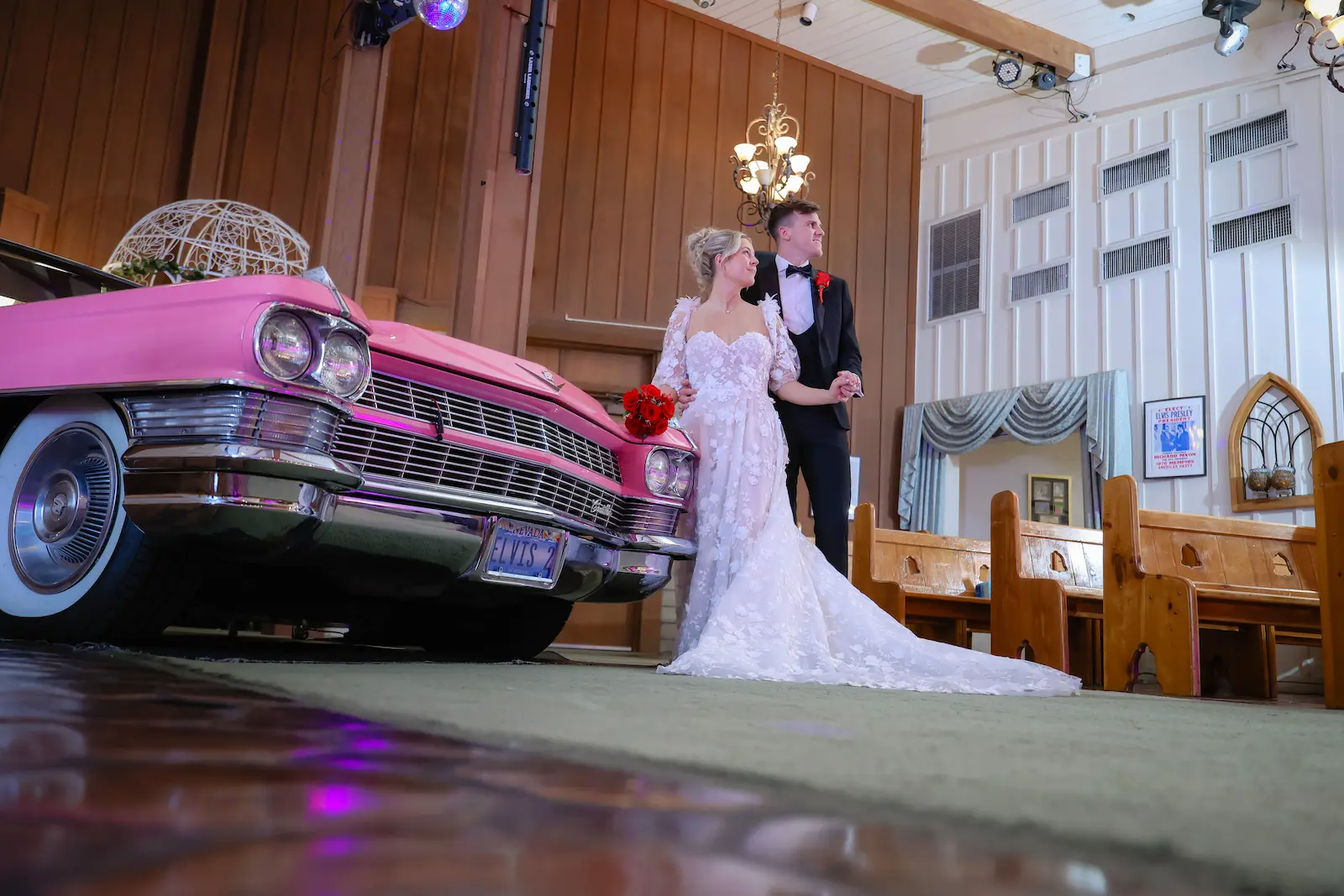 Bride and groom posing beside vintage pink Cadillac inside Viva Las Vegas Wedding Chapel