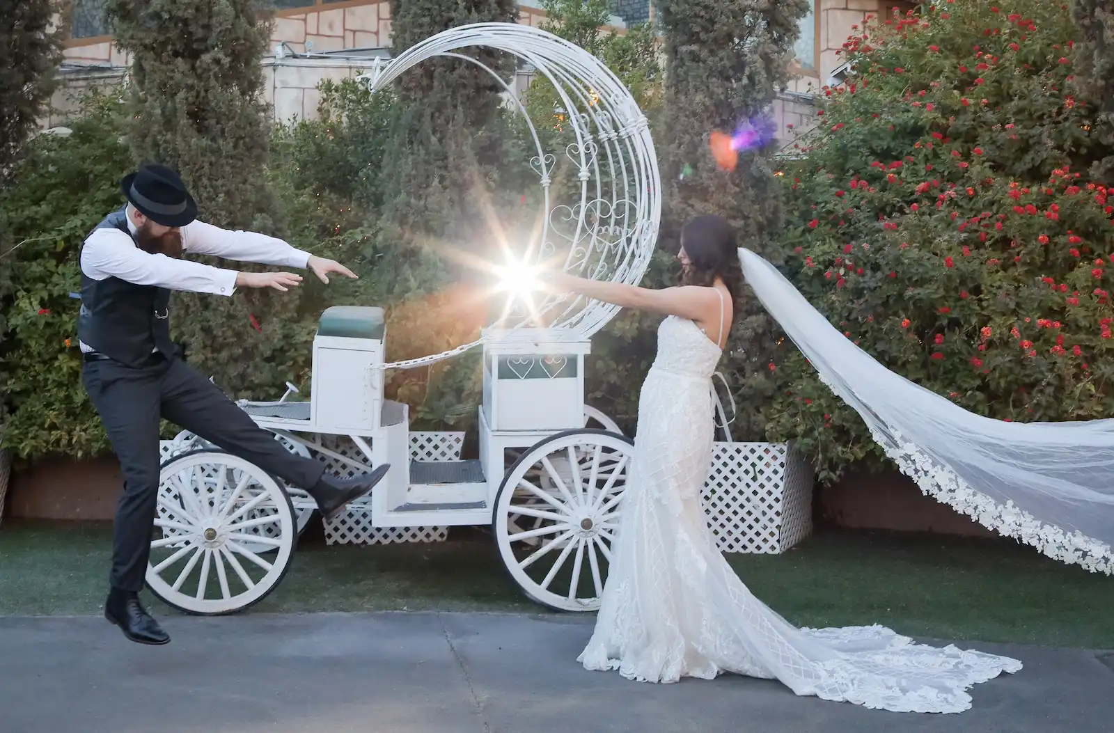 Bride with a flowing veil and groom playfully posing with a white Cinderella carriage and a magic light burst at a Las Vegas wedding venue.