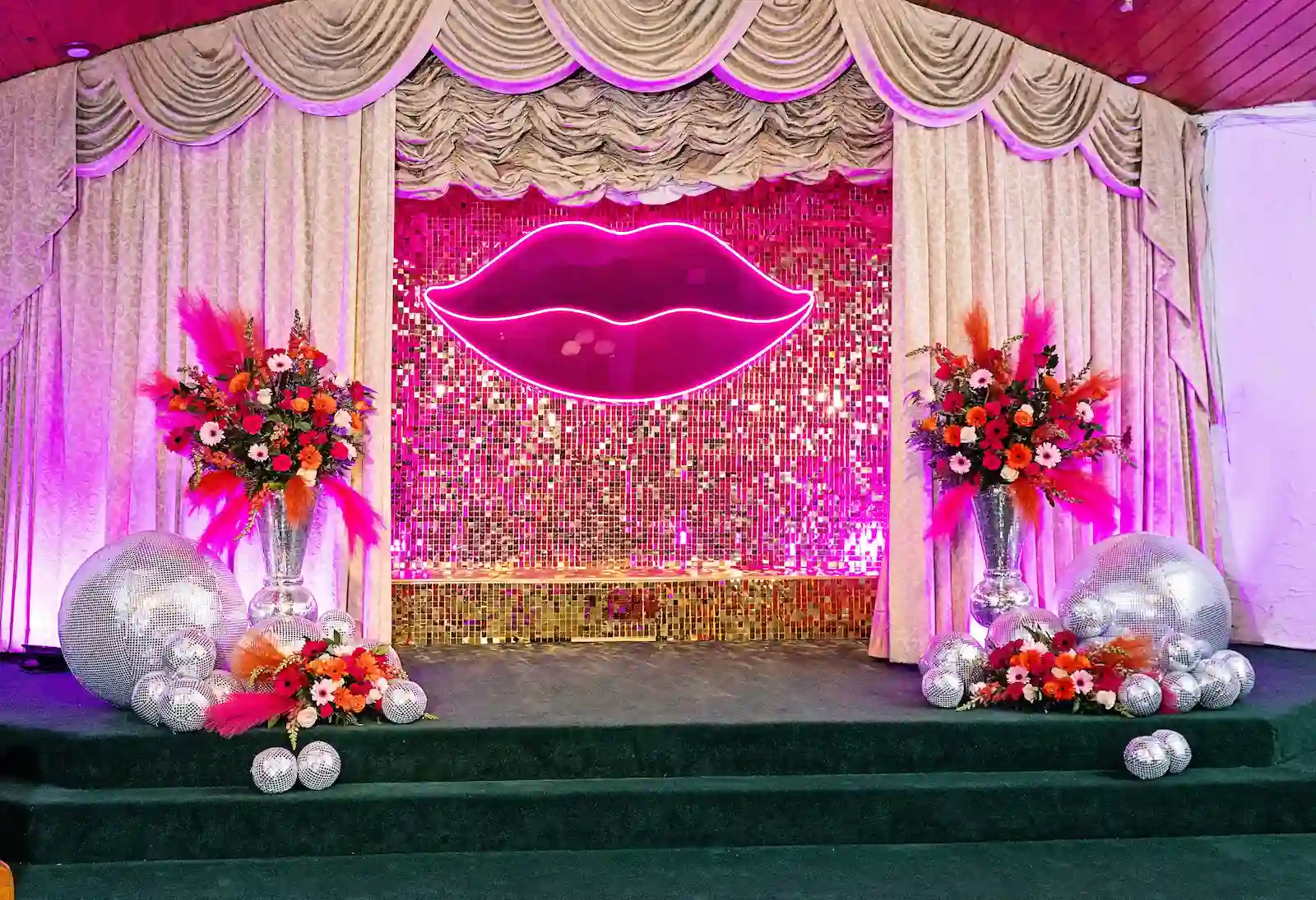 Full disco wedding decor setup with neon lips sign, pink and orange floral arrangements, disco balls, and feathers at Viva Las Vegas Weddings chapel