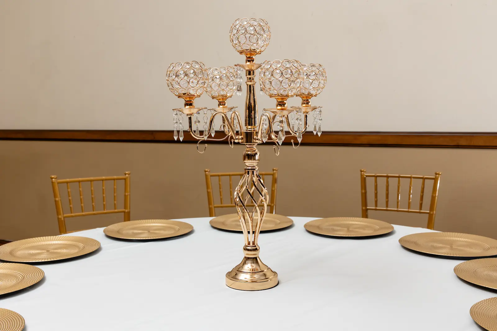 Gold five-arm crystal candelabra centerpiece on a white reception table with gold charger plates and chiavari chairs at Viva Las Vegas Weddings