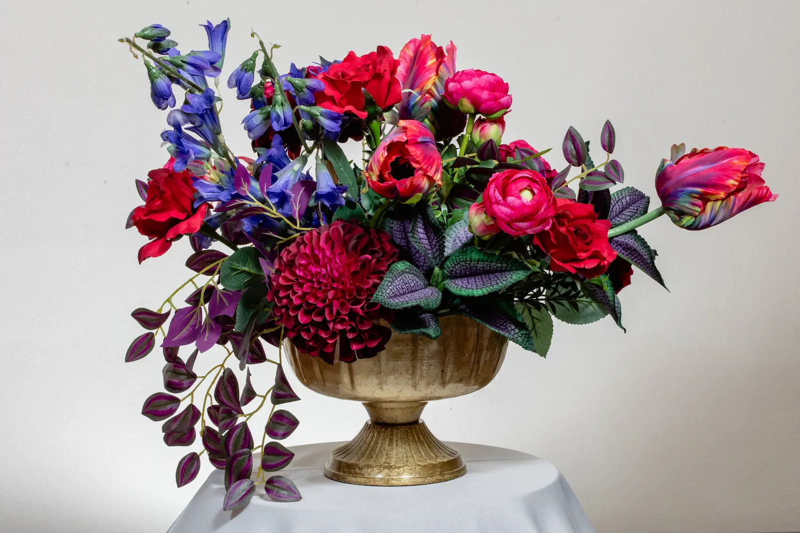 Silk jewel tone wedding centerpiece with red roses, magenta dahlia, parrot tulips, ranunculus, and purple bellflowers in a gold compote vase at Viva Las Vegas Weddings