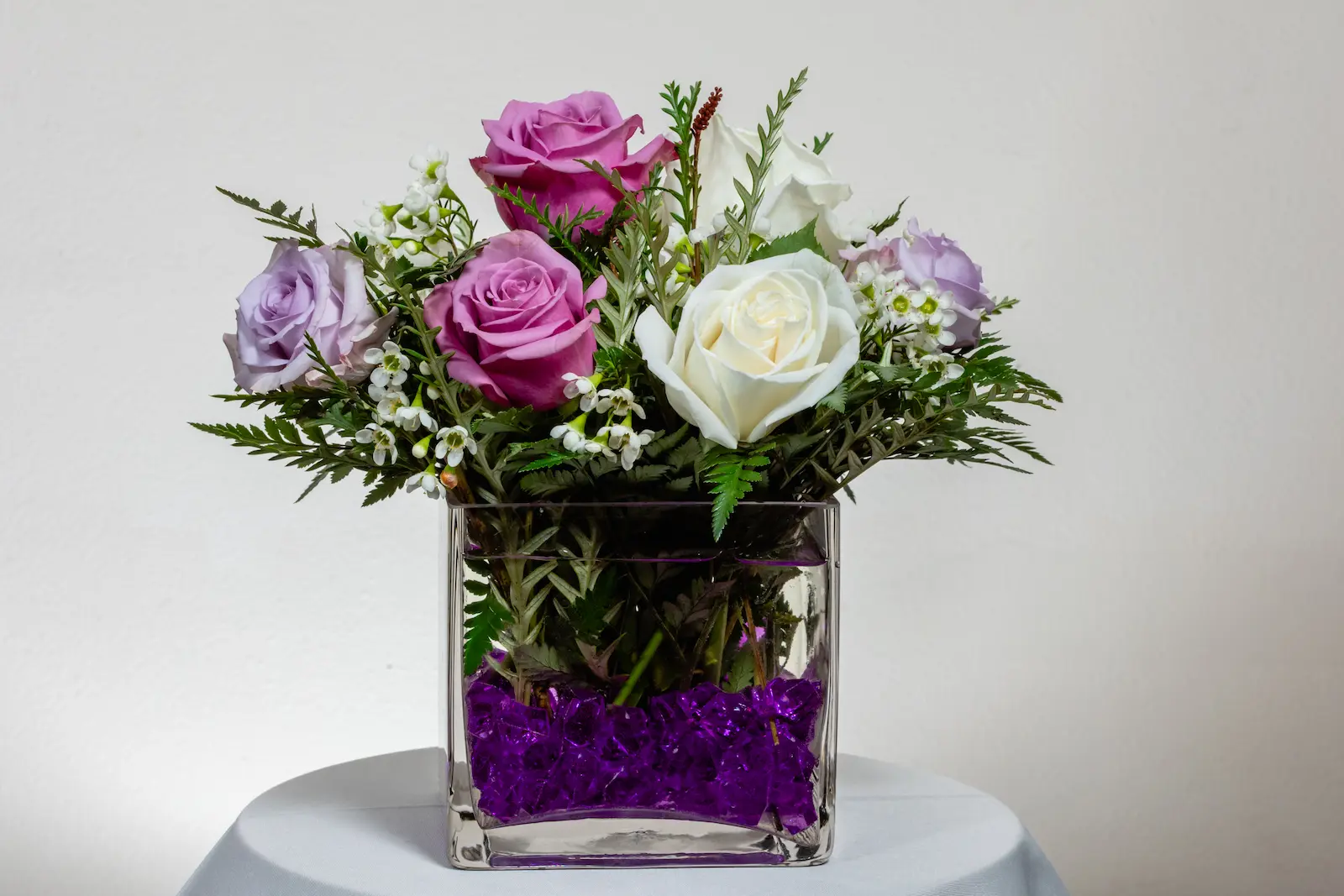Fresh rose reception centerpiece with lavender, pink, and white roses, waxflower, and fern in a glass cube vase at Viva Las Vegas Weddings