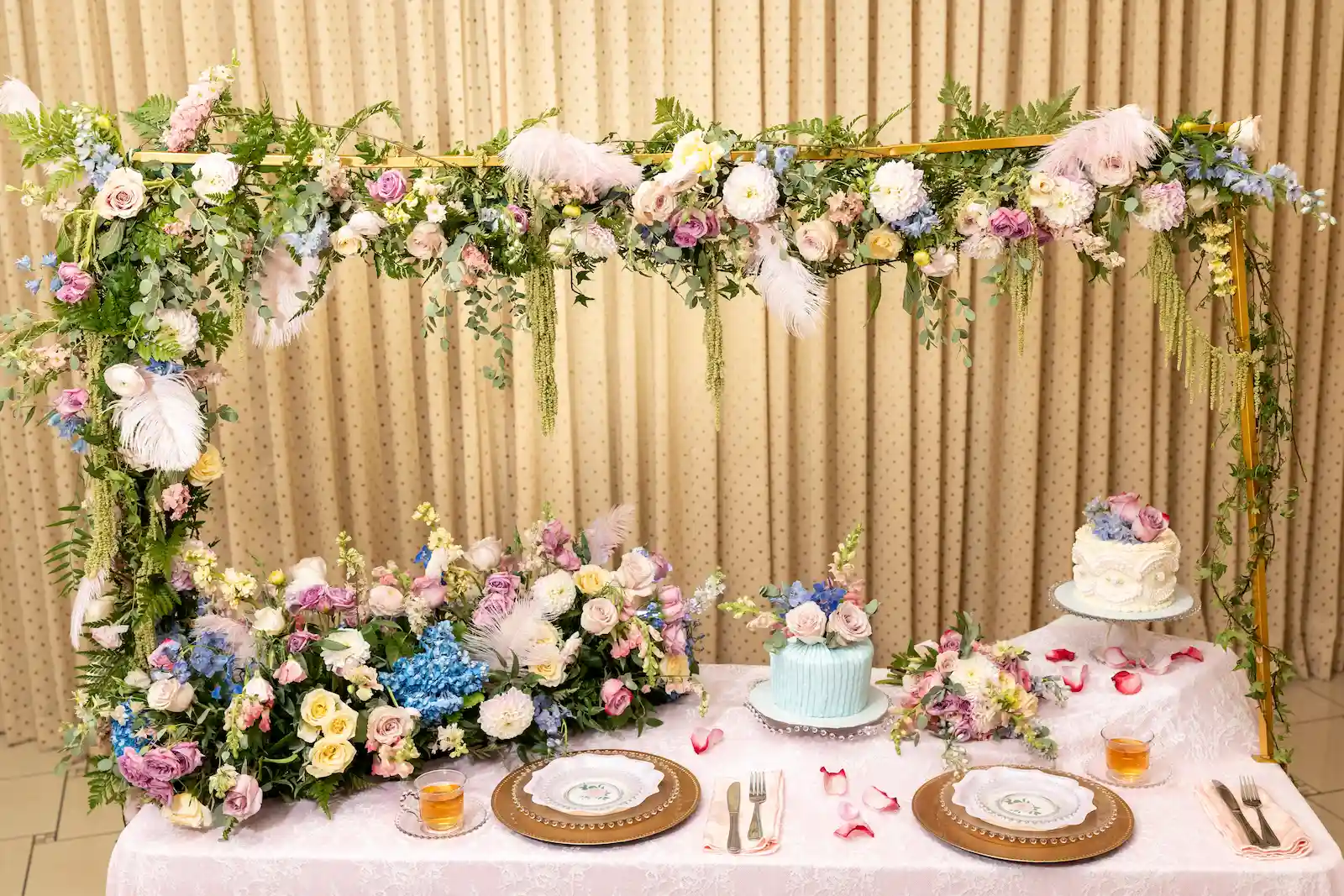 Bridgerton-inspired sweetheart table with a gold floral frame of pastel roses, dahlias, delphinium, and pink ostrich feathers, lace linen, and two tea-party cakes at Viva Las Vegas Weddings