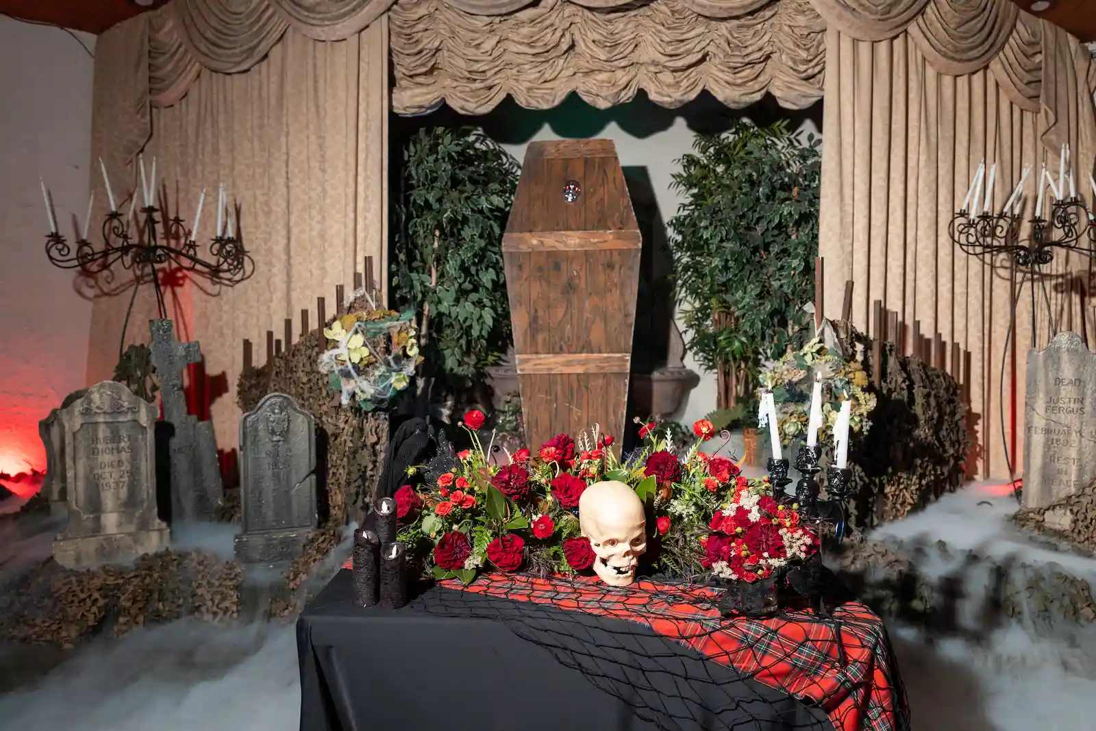 Maleficent-inspired gothic sweetheart table with red roses, burgundy dahlias, skull, black candles, and red tartan runner in a foggy graveyard setting with a coffin at Viva Las Vegas Weddings