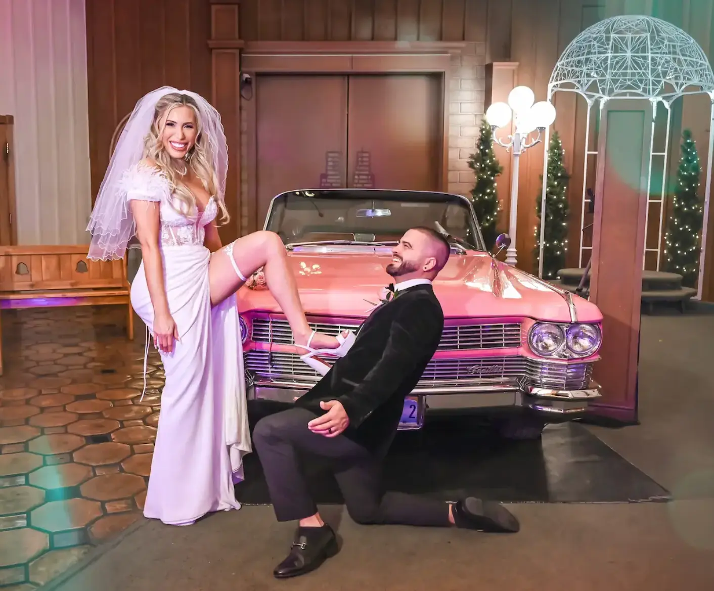 Bride and groom posing playfully with a vintage pink Cadillac inside a Las Vegas wedding chapel