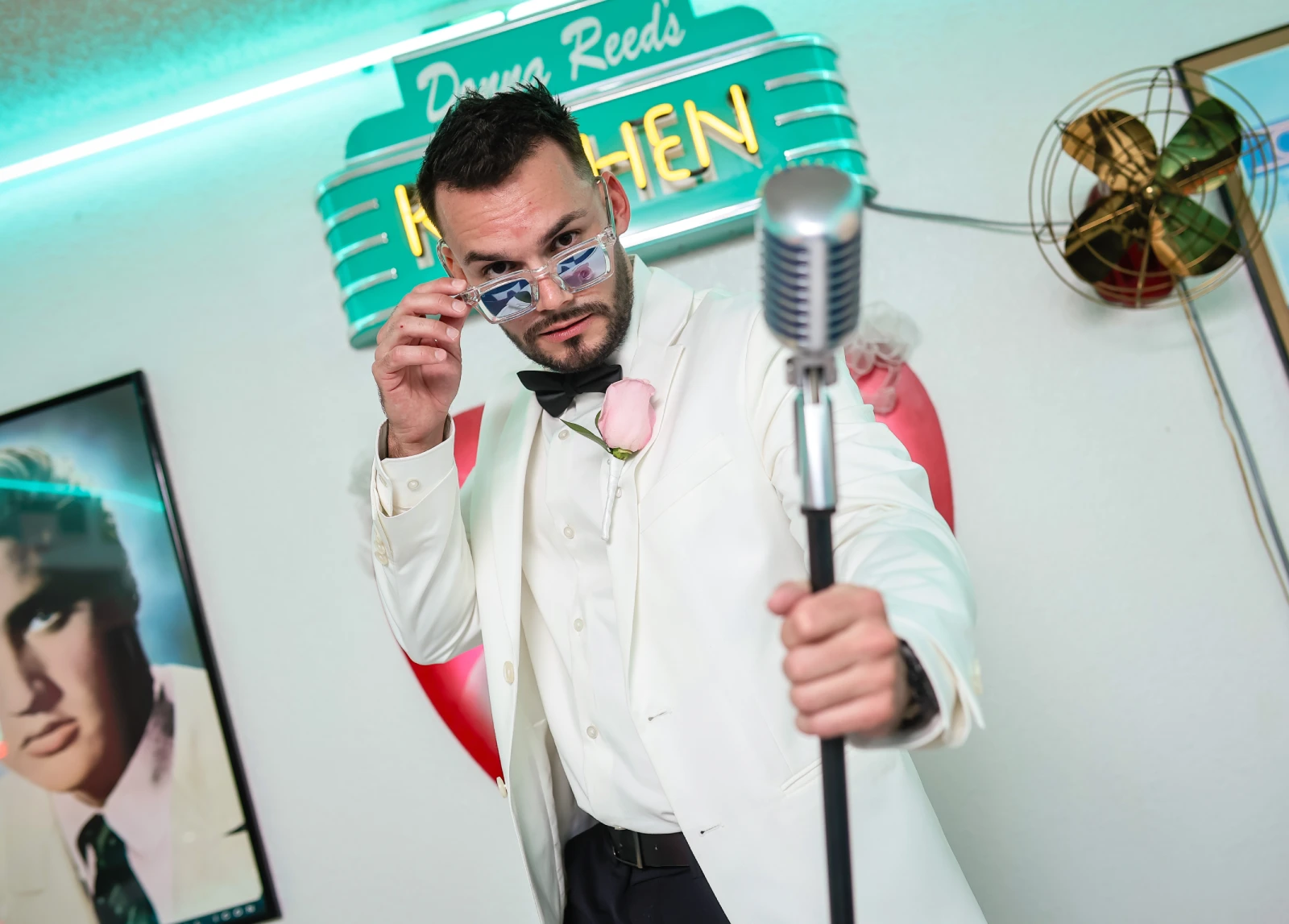Groom in white suit holding vintage microphone inside retro diner wedding chape