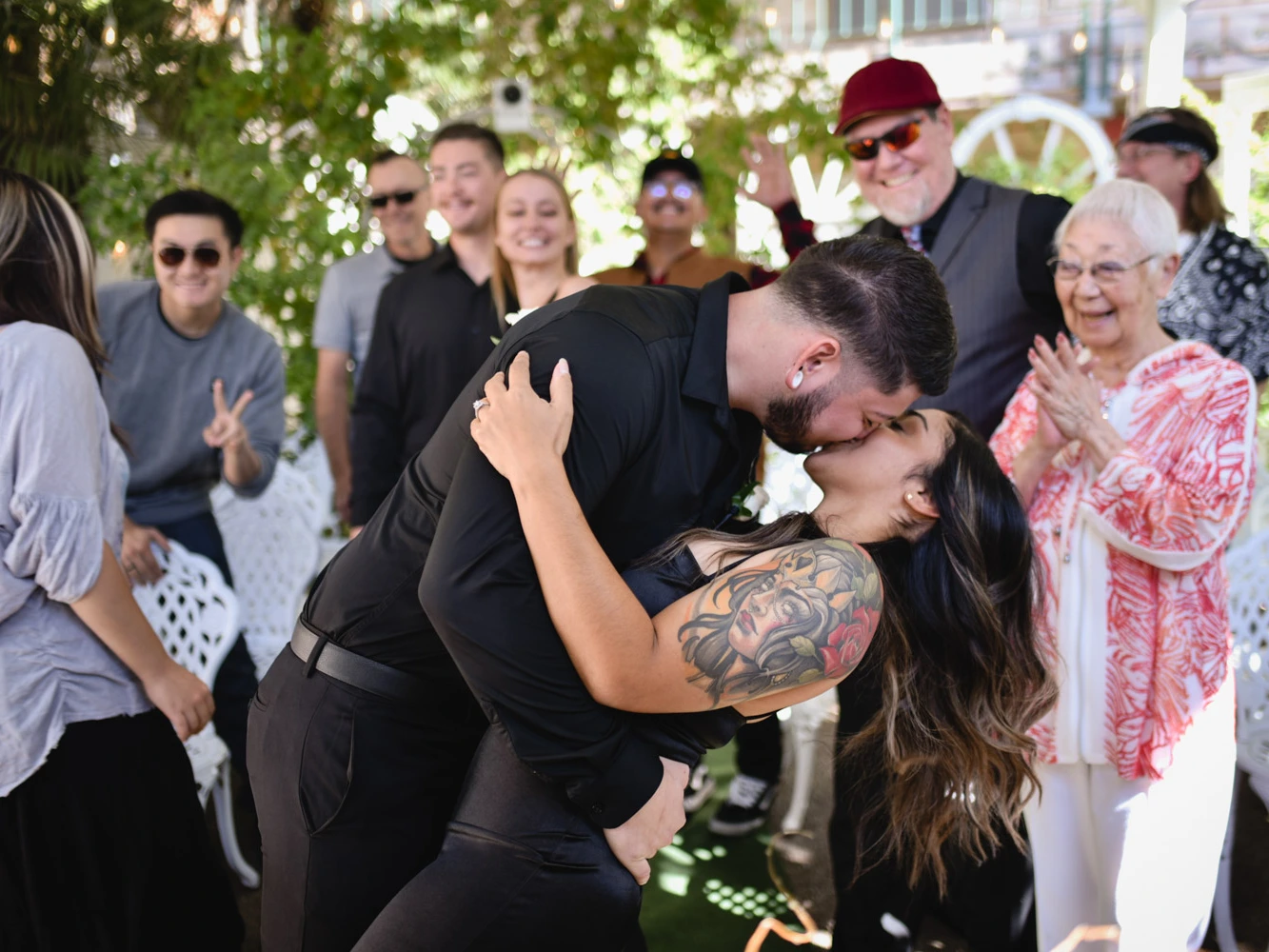 Couple sharing a romantic kiss during outdoor Las Vegas wedding ceremony surrounded by cheering family and friends.