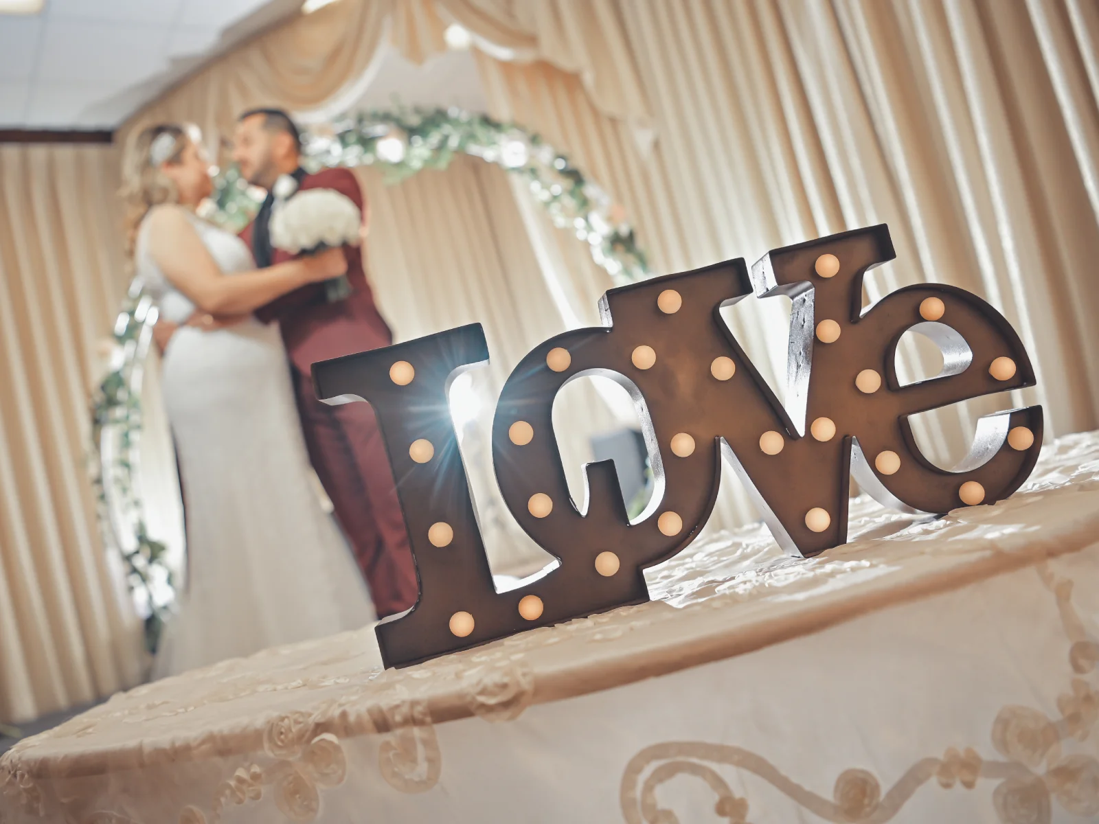 Illuminated LOVE sign in foreground with wedding couple softly blurred behind.