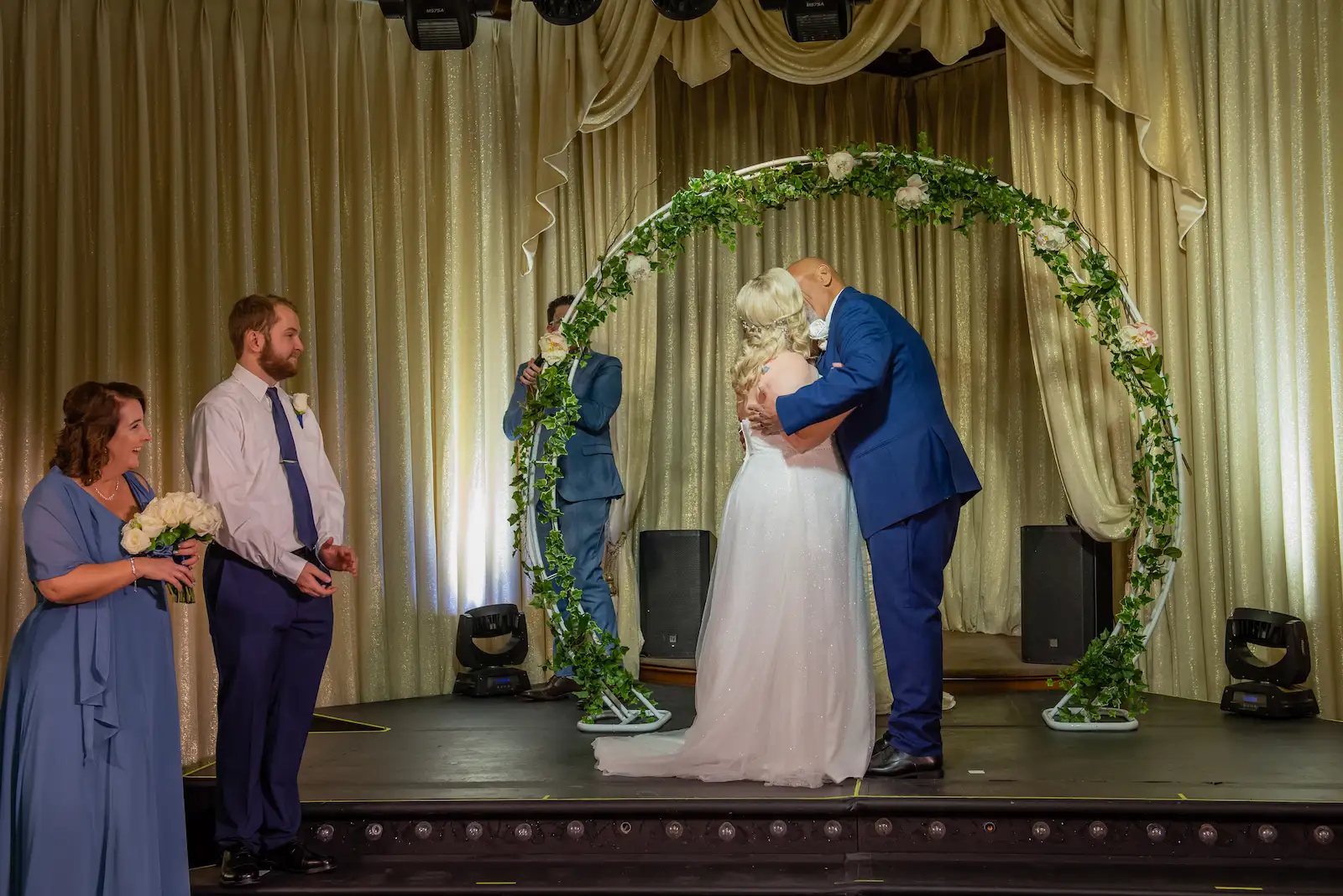 Bride and groom sharing first kiss under a greenery arch at a Las Vegas wedding reception ceremony