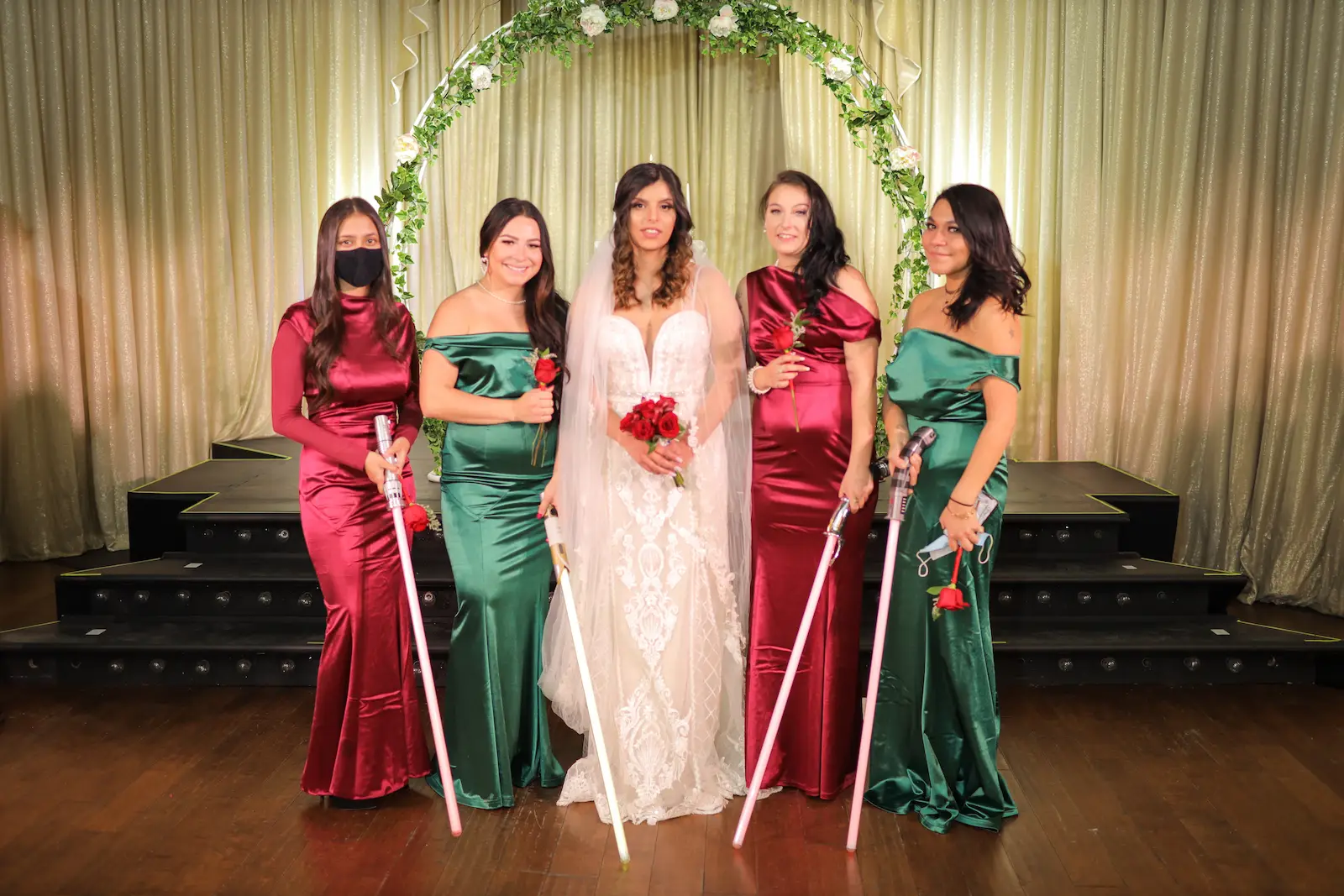 Bride with bridesmaids in red and green satin gowns holding lightsabers at a Las Vegas wedding reception