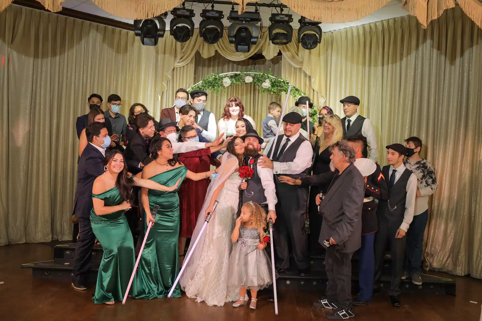 Large wedding party group photo with lightsabers under a floral arch at a Las Vegas wedding reception